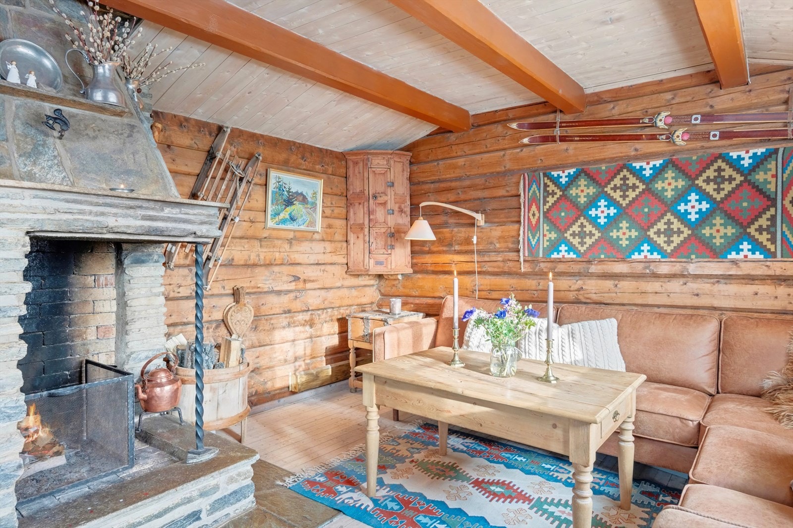 Romslig stue med synlige tømmervegger gir et ekstra hyttepreg. Stor åpen peis i naturstein gir effektiv oppvarming og setter den riktige stemningen. Galleribilde