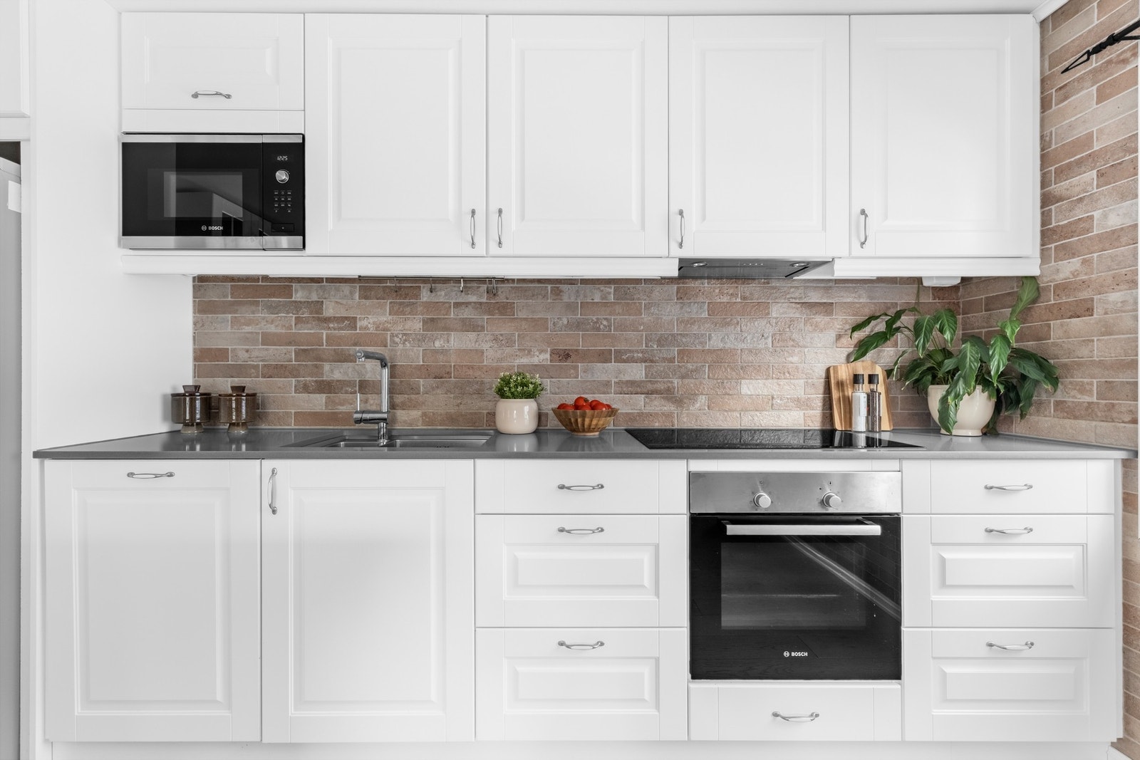 Hvite profilerte fronter kombinert med grå kvartsitt benkeplate, flislagt vegg og praktisk belysning under overskap gir et stilrent uttrykk. Galleribilde