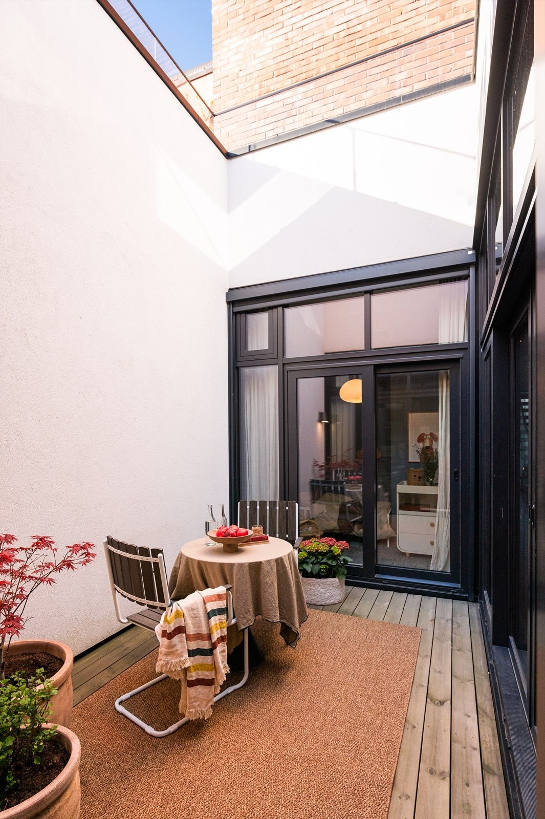 Atriet har terrassebord i tre og er møblert med en hyggelig sittegruppe og dekorative plantekasser som gir en varm og innbydende stemning. Galleribilde