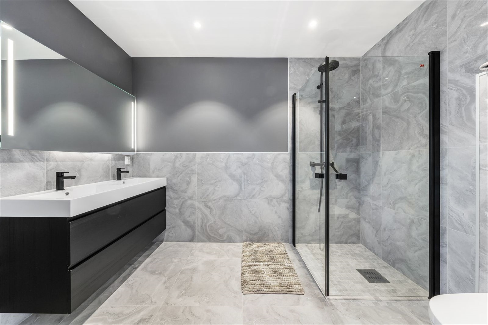 Badet i 2. etasje er romslig og lekkert med flis på gulv og delvis på vegger. Her er det vegghengt spyletoalett, VikingBad, Rainshower som leveres med termostatstyrt dusjblander med dusjdør og baderomsinnredning fra VikingBad. Elektrisk varme i gulv. Galleribilde