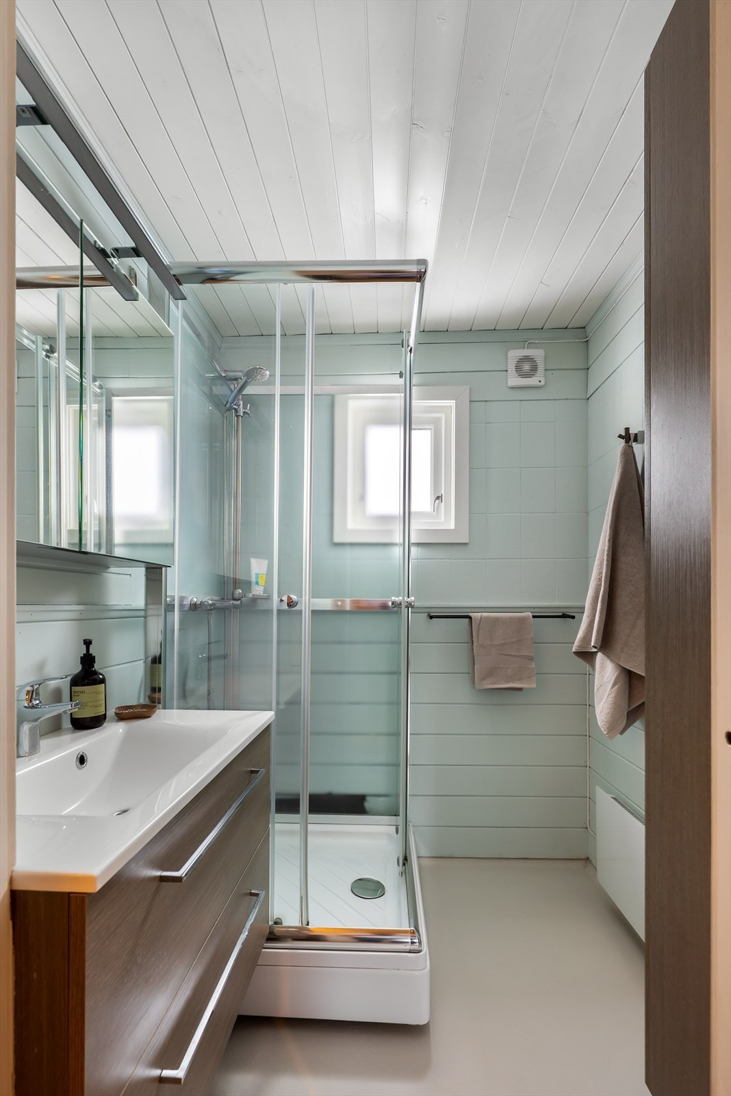 Badet er utstyrt med dusjkabinett og mekanisk avtrekk, med panel og tapet på vegger. Galleribilde