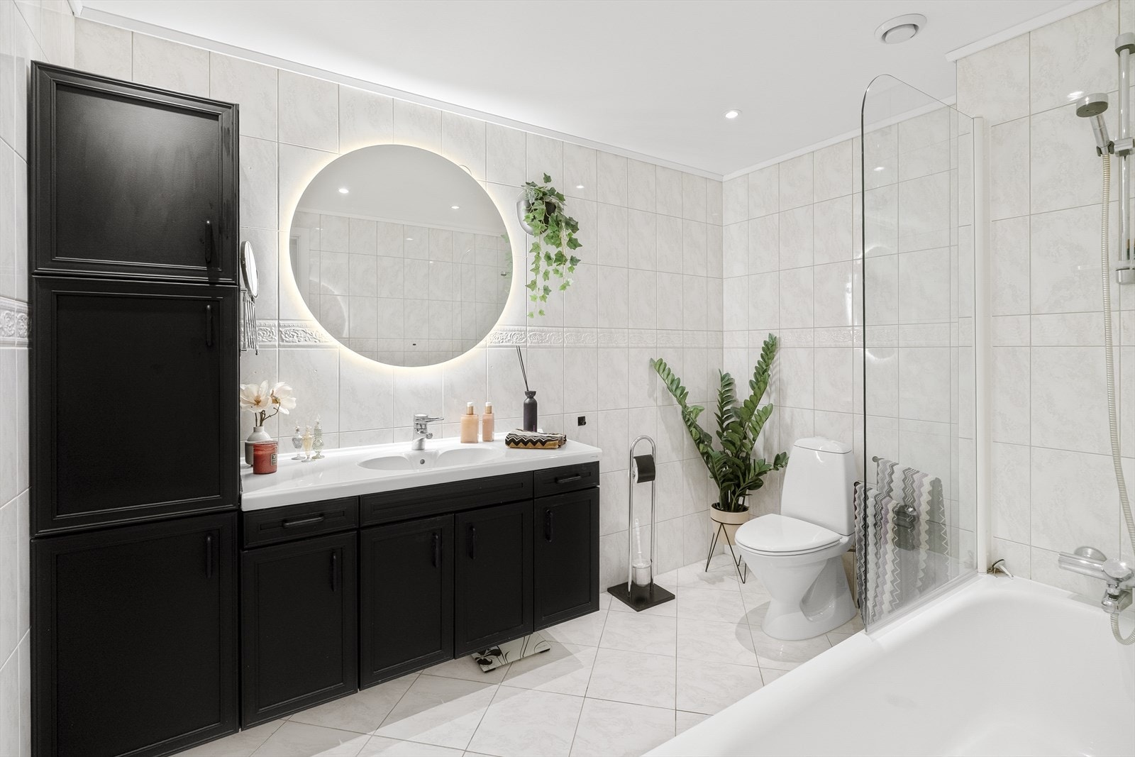 Baderommet fremstår tidløst og stilrent med fliser på gulv og vegger og er utstyrt med servant, toalett og badekar med dusjløsning. Galleribilde