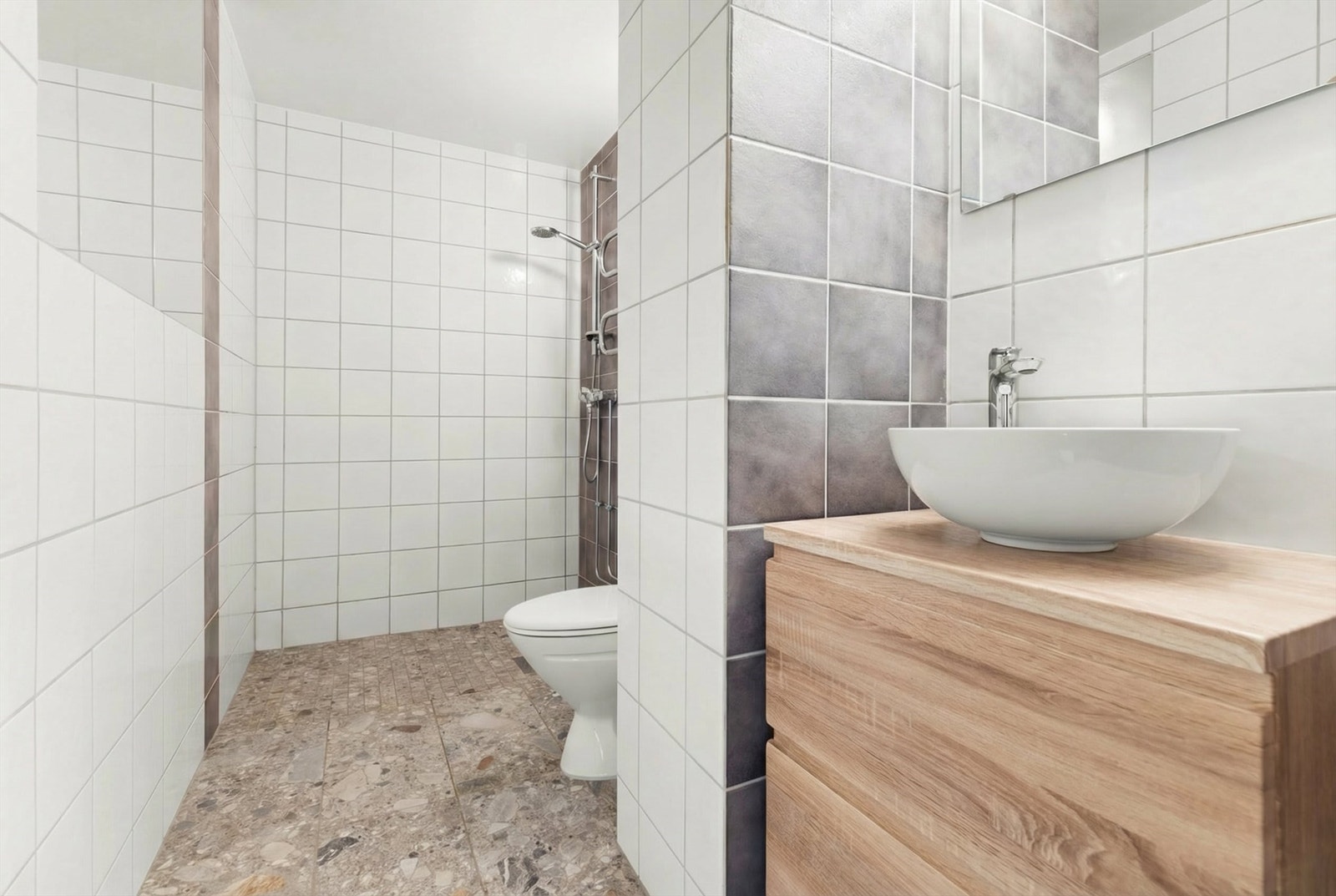 Badet er flislagt på gulv og vegger med elektrisk gulvvarme. Innredet med klosett, servant plassert på innredning, innfelt speil og dusjhjørne. Opplegg for vaskemaskin. Galleribilde