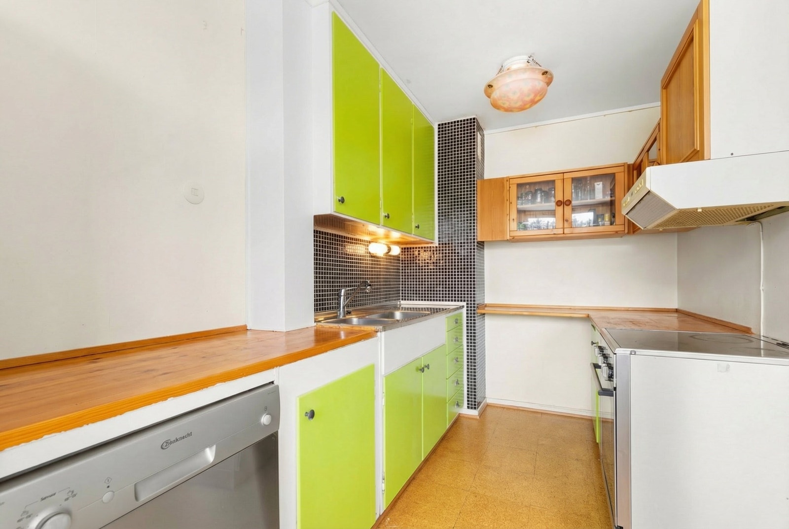 Kjøkkeninnredning med glatte fronter og stålbeslag med nedfelt vask- og skyllekum, og heltre benkeplate. Fliser over deler av benkeplaten. Det er opplegg for komfyr og oppvaskmaskin. Galleribilde