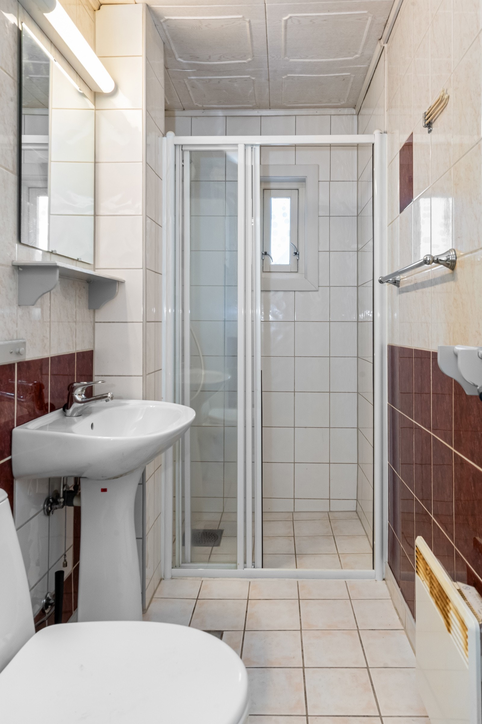 Eldre våtrom med fliser på gulv og vegger. Det er montert dusjvegg, søyleservant og toalett. Galleribilde