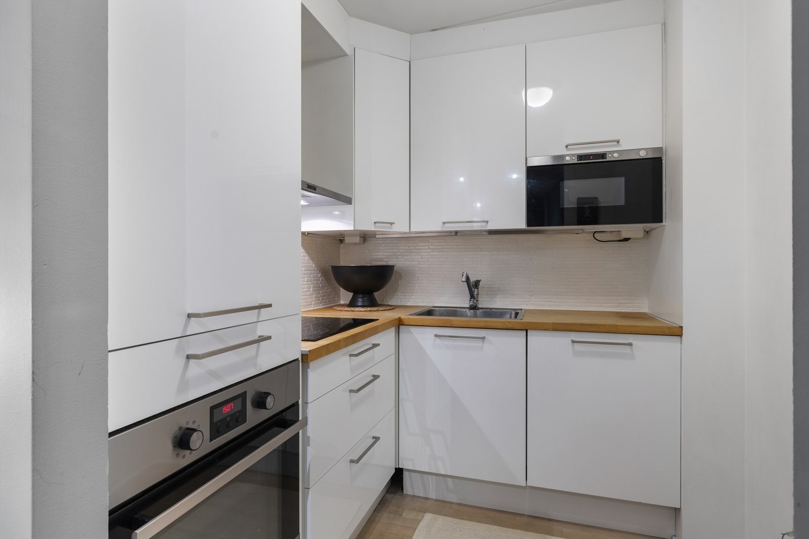 Kjøkken med glatte høyglans fronter. Heltre benkeplate med nedfelt vaskekum og keramisk platetopp. Malte fliser over benk. Integrert stekeovn, mikro, oppvaskmaskin og kjøleskap m/fryseboks. Galleribilde