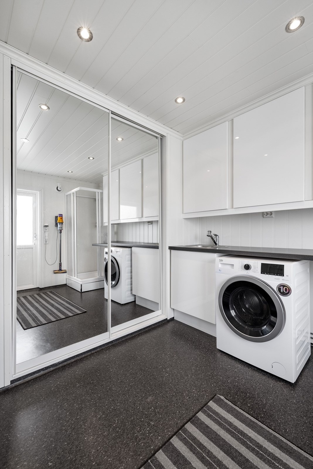 Rikelig med oppbevaringsplass i romslig plassbygget skyvedørsgarderobe med speildører. Det er også flott vaskeromsinnredning med vask og opplegg for vaskemaskin under benkeplate, samt dusjkabinett. Galleribilde