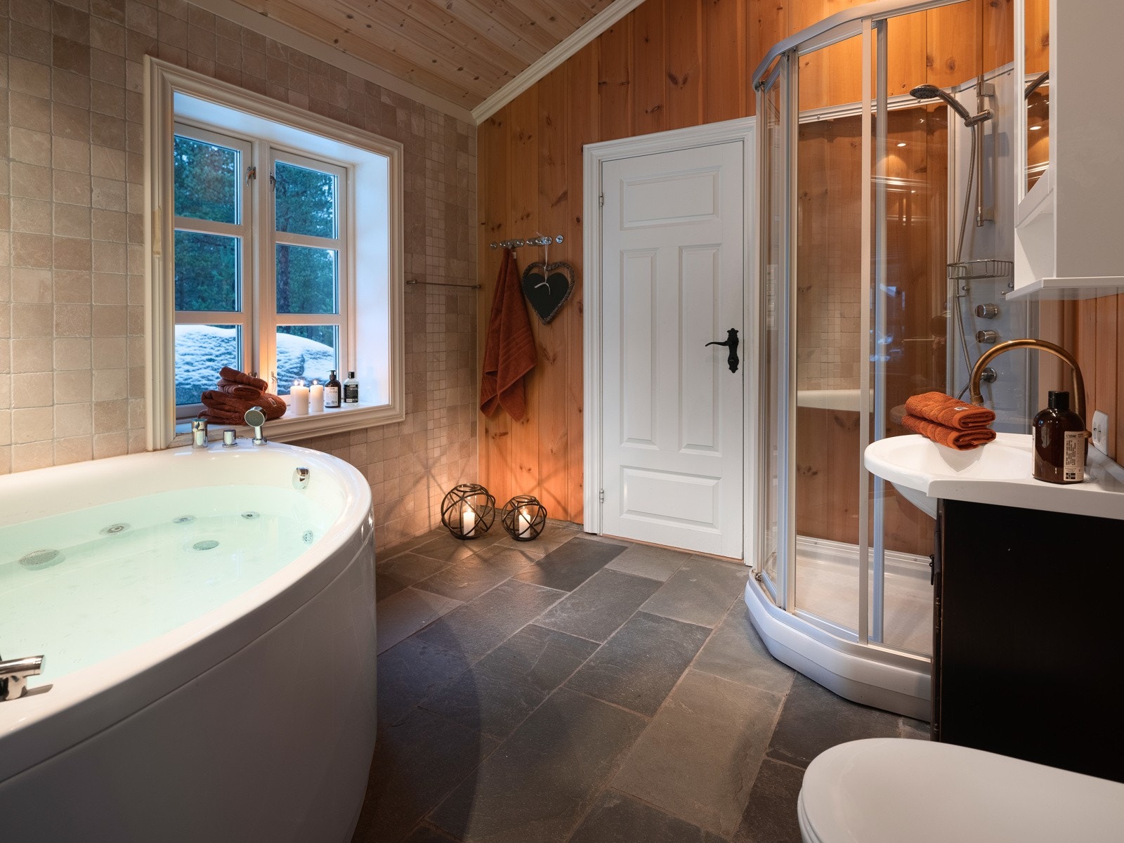 Badet har flislagt gulv og stort badekar og dusj Galleribilde