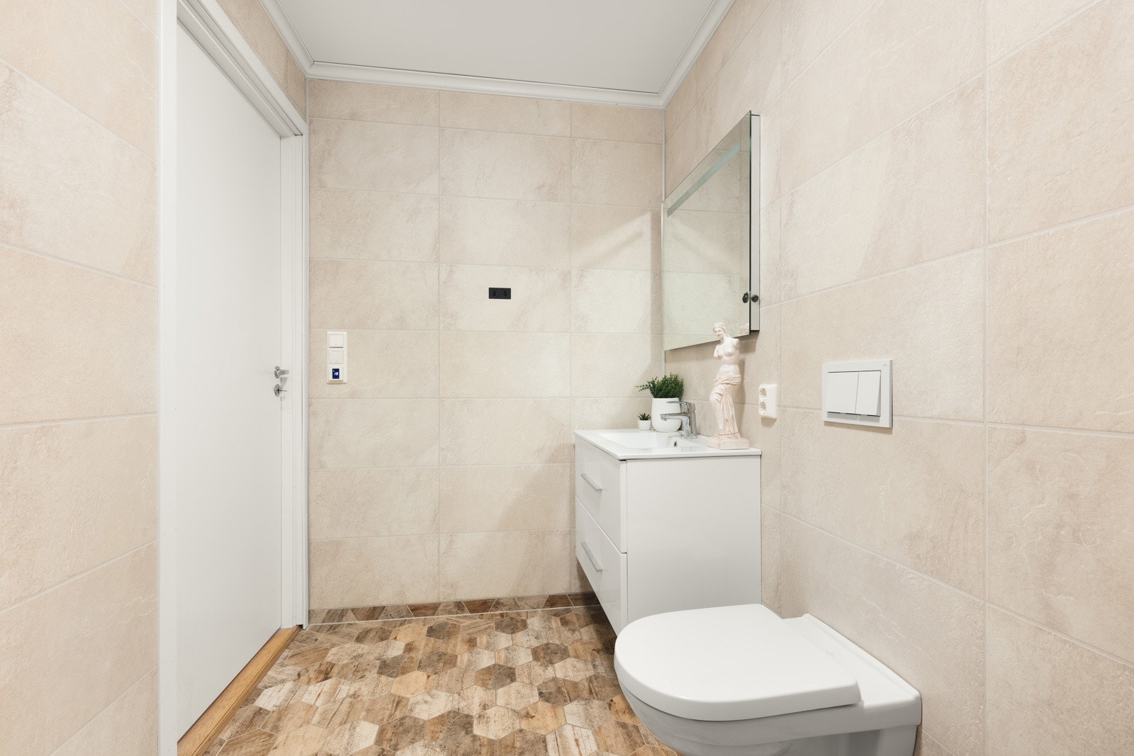 Pent bad med flislagt gulv med varme og baderomsplater på vegger. Rommet har moderne innredning med nedfelt servant, veggmontert toalett samt dusjhjørne med glassvegger. Et lyst og praktisk baderom med tidløs standard. Galleribilde