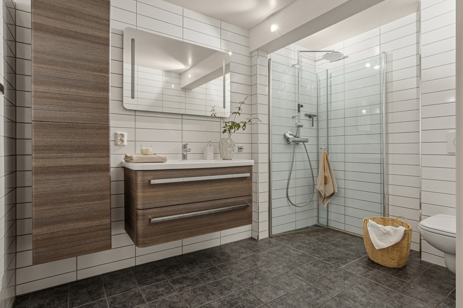 Romslig baderomsinnredning med godt lagringsrom og et stort speil med belysning gjør badet både praktisk og elegant. Flislagt gulv med varmekabler sørger for komfort året rundt. Galleribilde