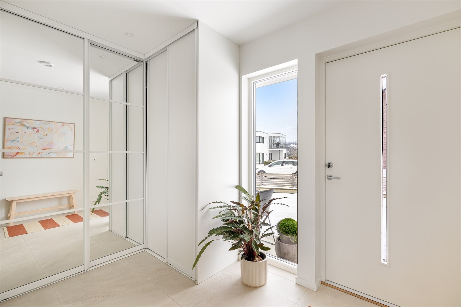 En lys og innbydende entré/gang med 60x60 fliser på gulv og hvitmalte vegger. Det er varmekabler i gulvet og downlights i himlingen, noe som gir både komfort og et moderne uttrykk. Galleribilde