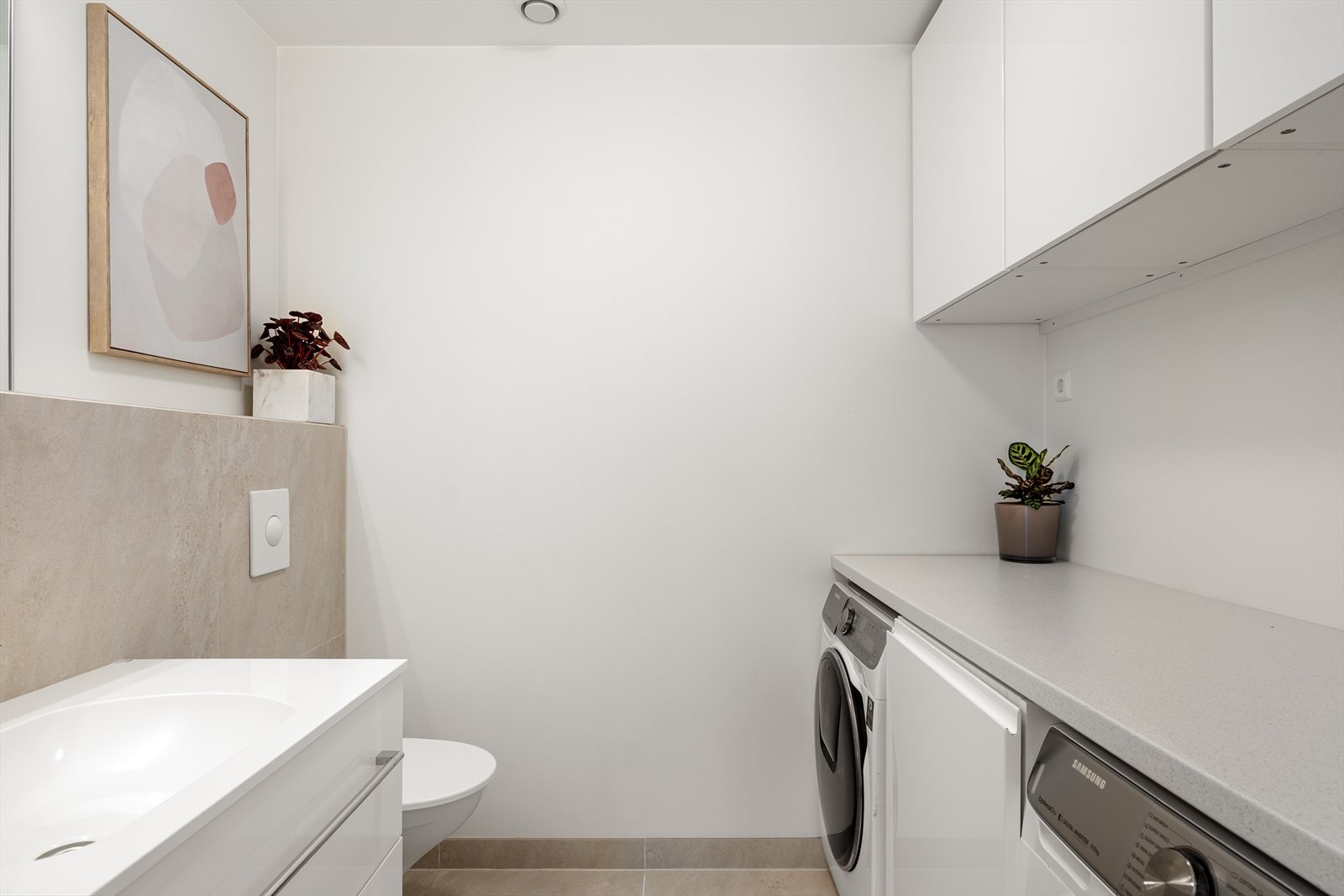 Vaskerommet er praktisk innredet med vegghengt toalett, servant i seksjon med speil, samt skap- og benkeplass. Det er opplegg for vaskemaskin og tørketrommel, noe som gir en effektiv og gjennomtenkt løsning for en enkel hverdag. Galleribilde