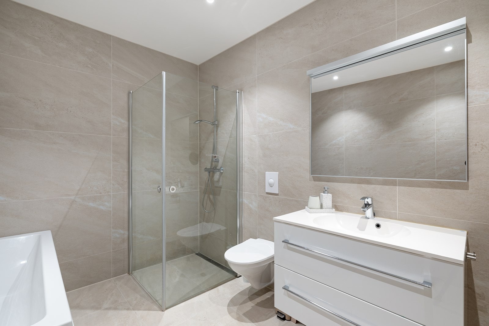 Badet er innredet med vegghengt toalett, servant i seksjon, dusjhjørne og badekar. Galleribilde