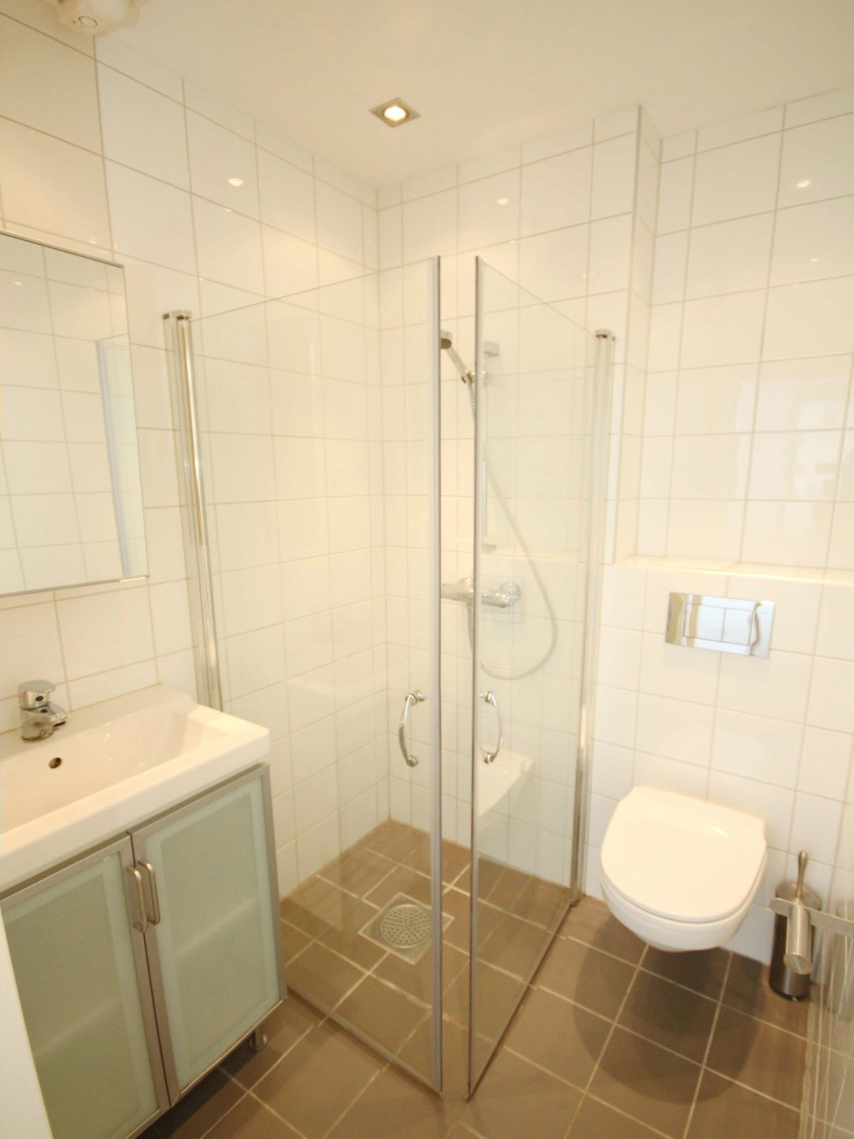 Pent flislagt bad med vegghengt wc, dusjhjørne og servant med speil og skap Galleribilde