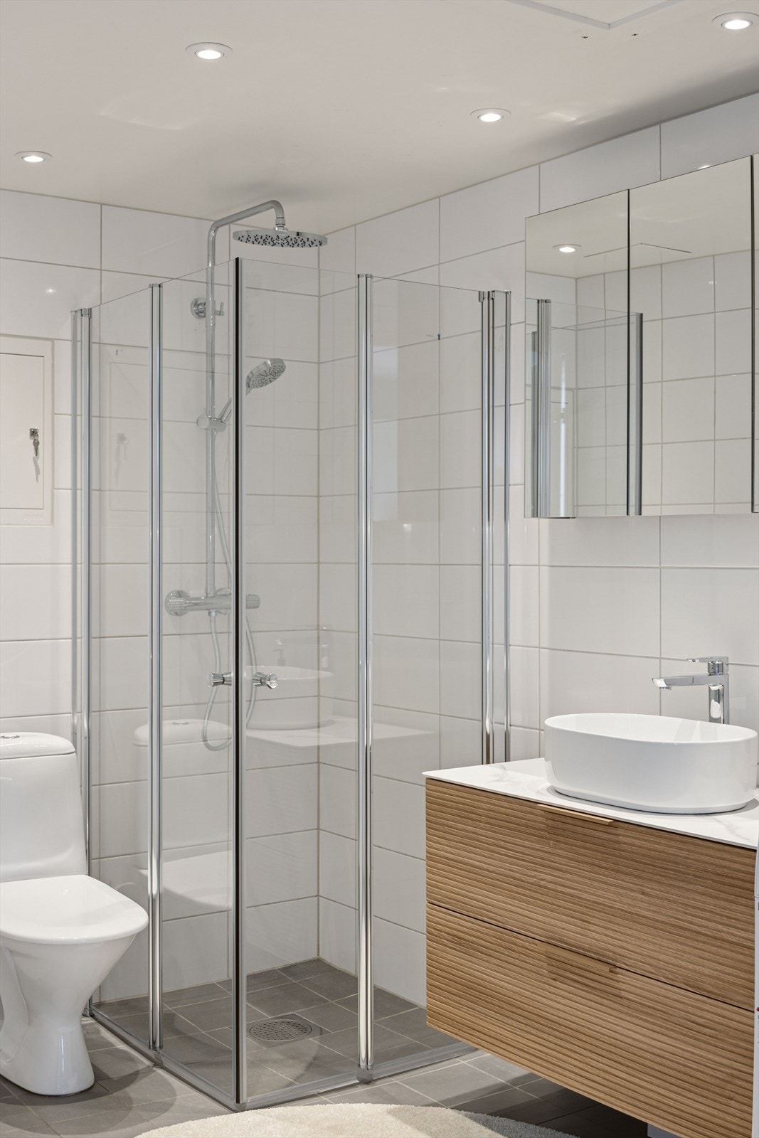 Badet er utstyrt med gulvmontert toalett, dusjhjørne med innfellbare glassdører (nye dusjdører fra 2026) og bolleservant med ettgreps blandebatteri (ny 2026). Galleribilde