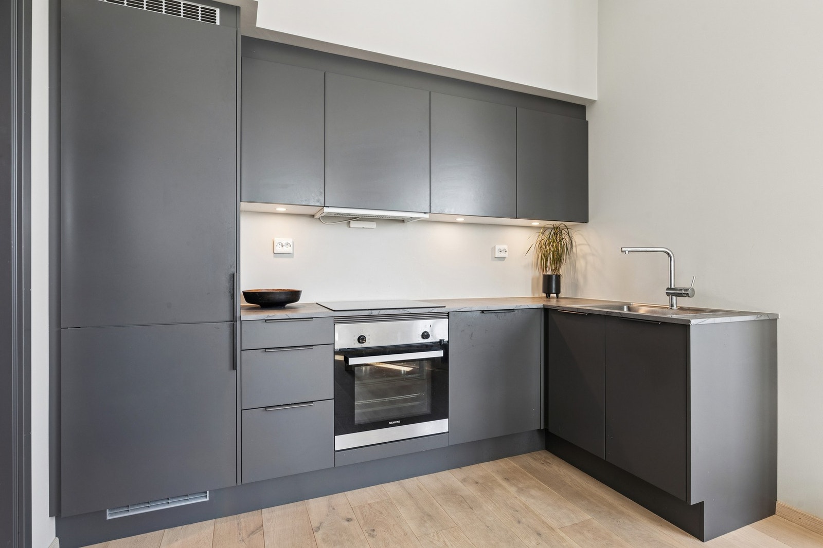 Innredningen har grå, glatte fronter med praktisk arbeidslys mellom overskap og benkeplate. Galleribilde