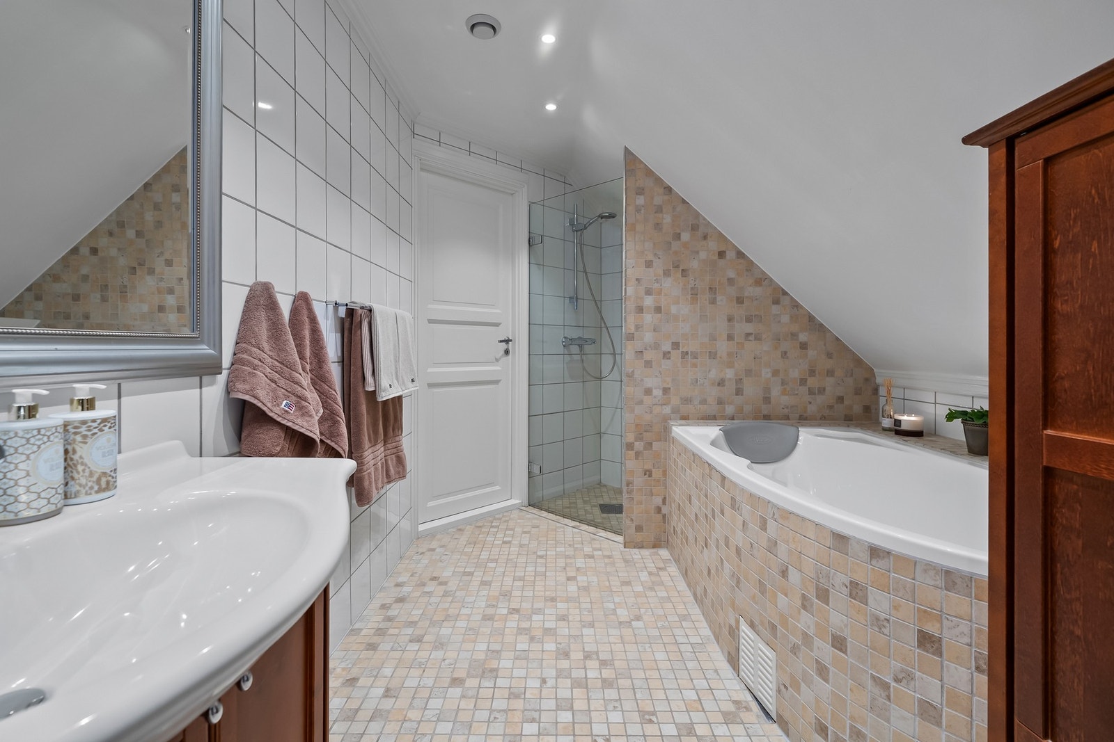 Badet har badekar med flislagt front, separat dusjløsning, toalett og servantinnredning med god oppbevaringsplass. Skråhimling og vindu tilfører karakter og naturlig lys, mens downlights gir en behagelig belysning. Galleribilde