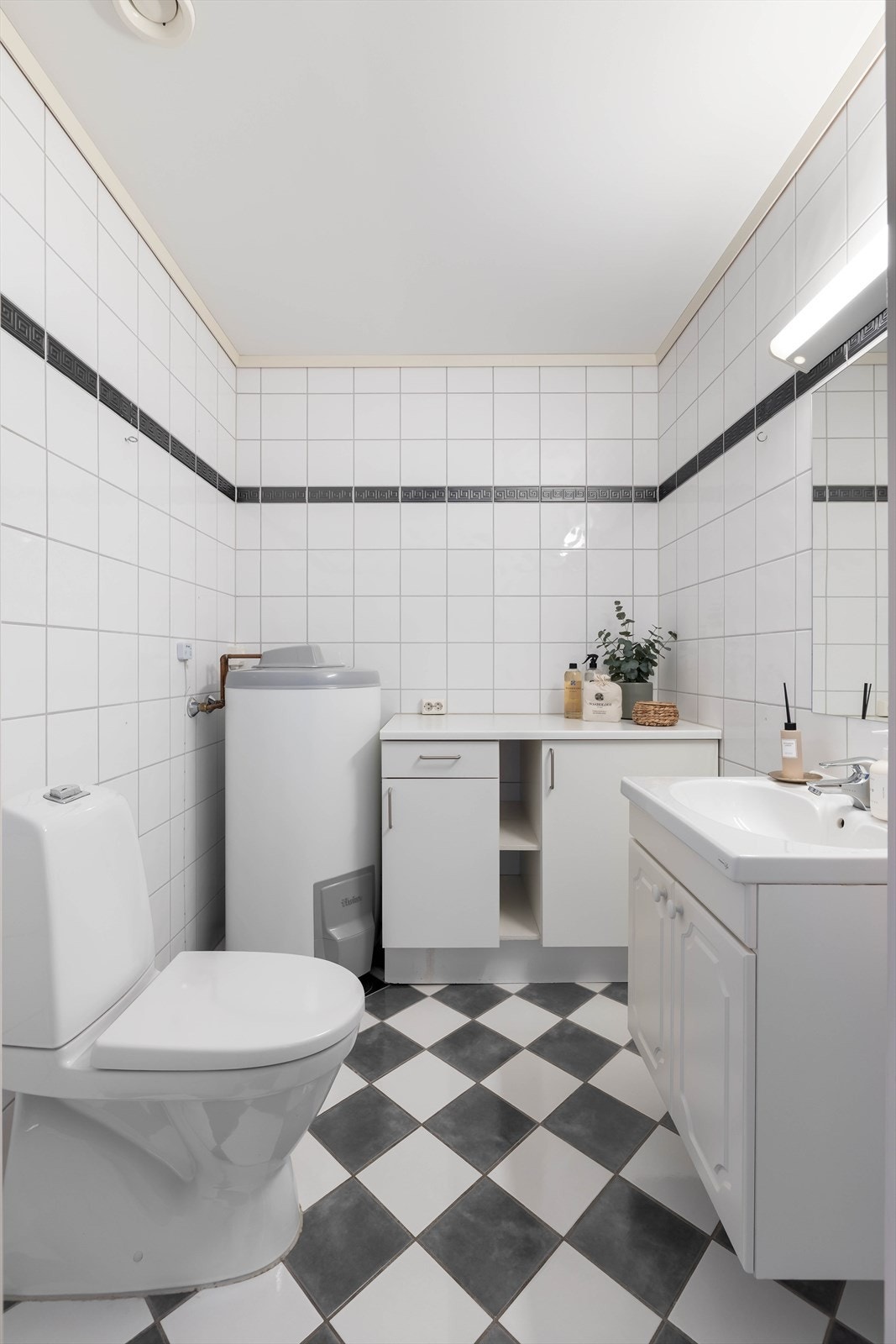 Baderom nr. to som er av noe mindre størrelse har også fliser på gulv og vegger, og inneholder gulvmontert toalett og innredning med servant. Her er også boligens varmvannsbereder på 200 liter plassert. Galleribilde