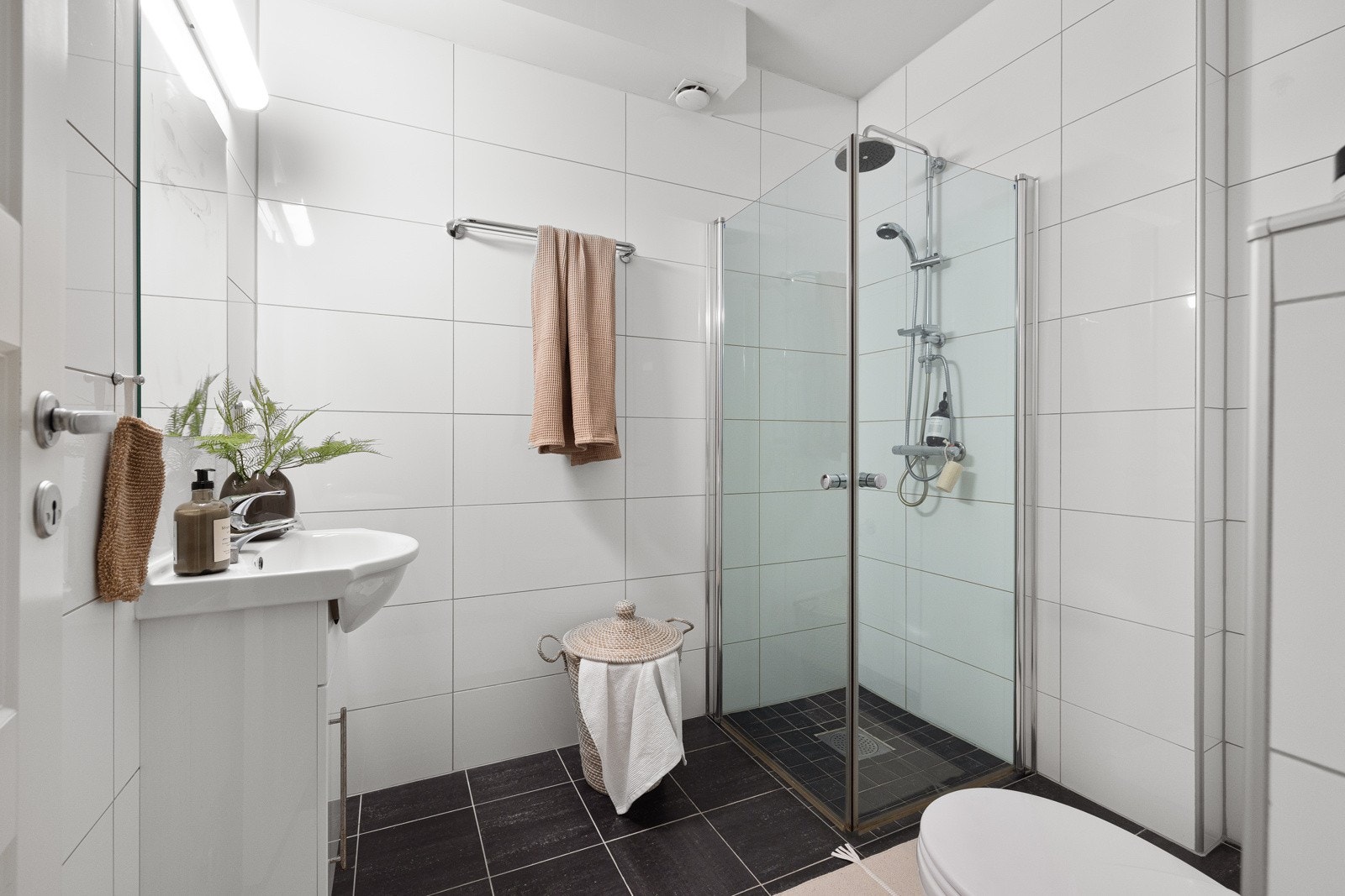 Toalettet er veggmontert, og dusjhjørnet er utstyrt med glassdører samt ettgreps dusjbatteri i rustfritt stål, med både håndholdt dusjhode og regnfallsdusj. Galleribilde