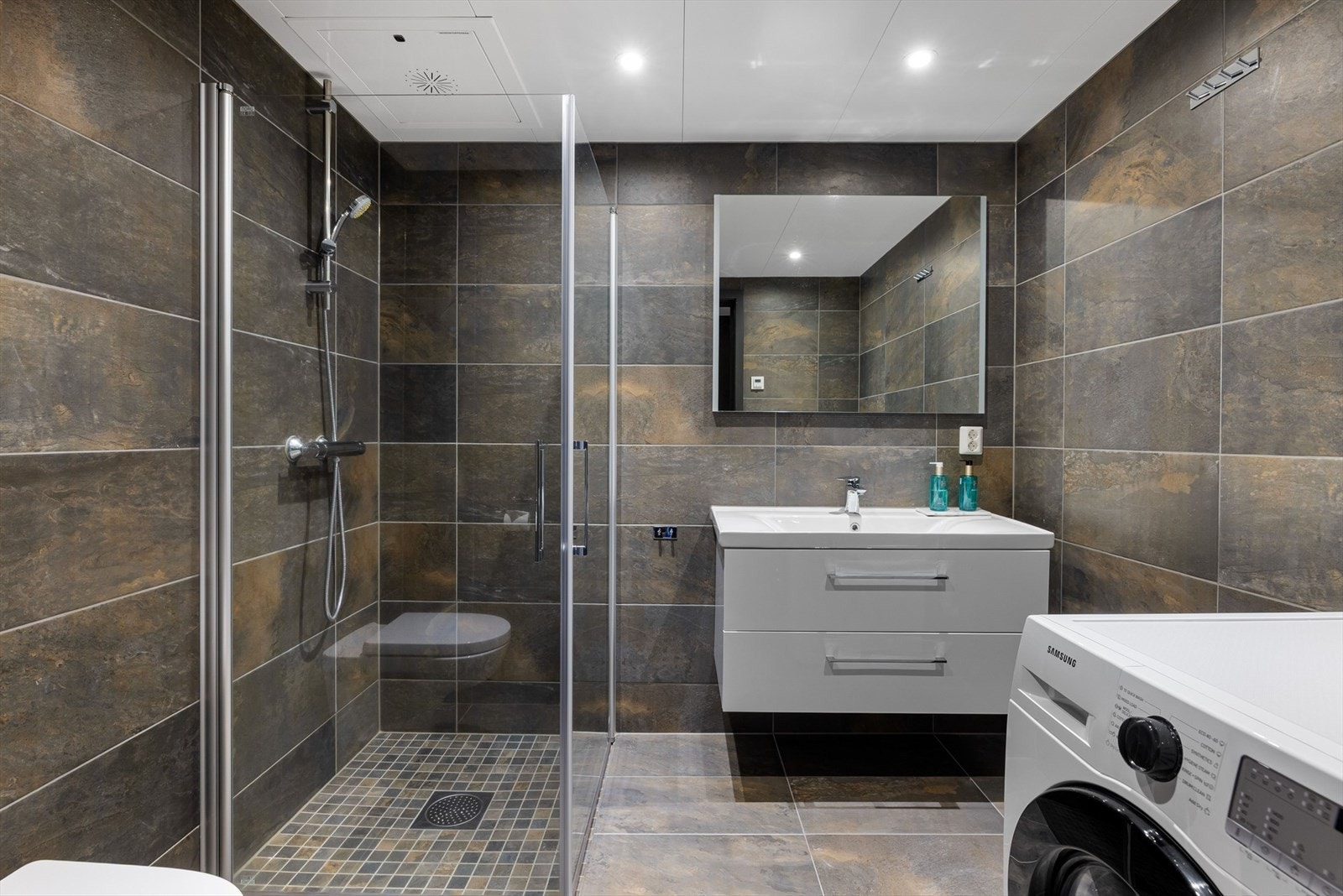 Baderom 2 er også innredet med dusjhjørne med glassvegger, servant på innredning og vegghengt toalett. Opplegg for vaskemaskin. Galleribilde