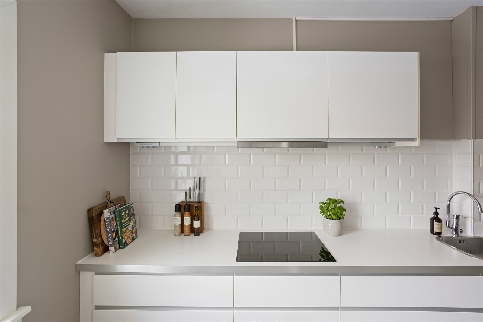 Innredningen har glatte folierte fronter, benkeplate i laminat med nedfelt kum i rustfritt stål, fliser på vegg over benk og ventilator med kullfilter. Galleribilde