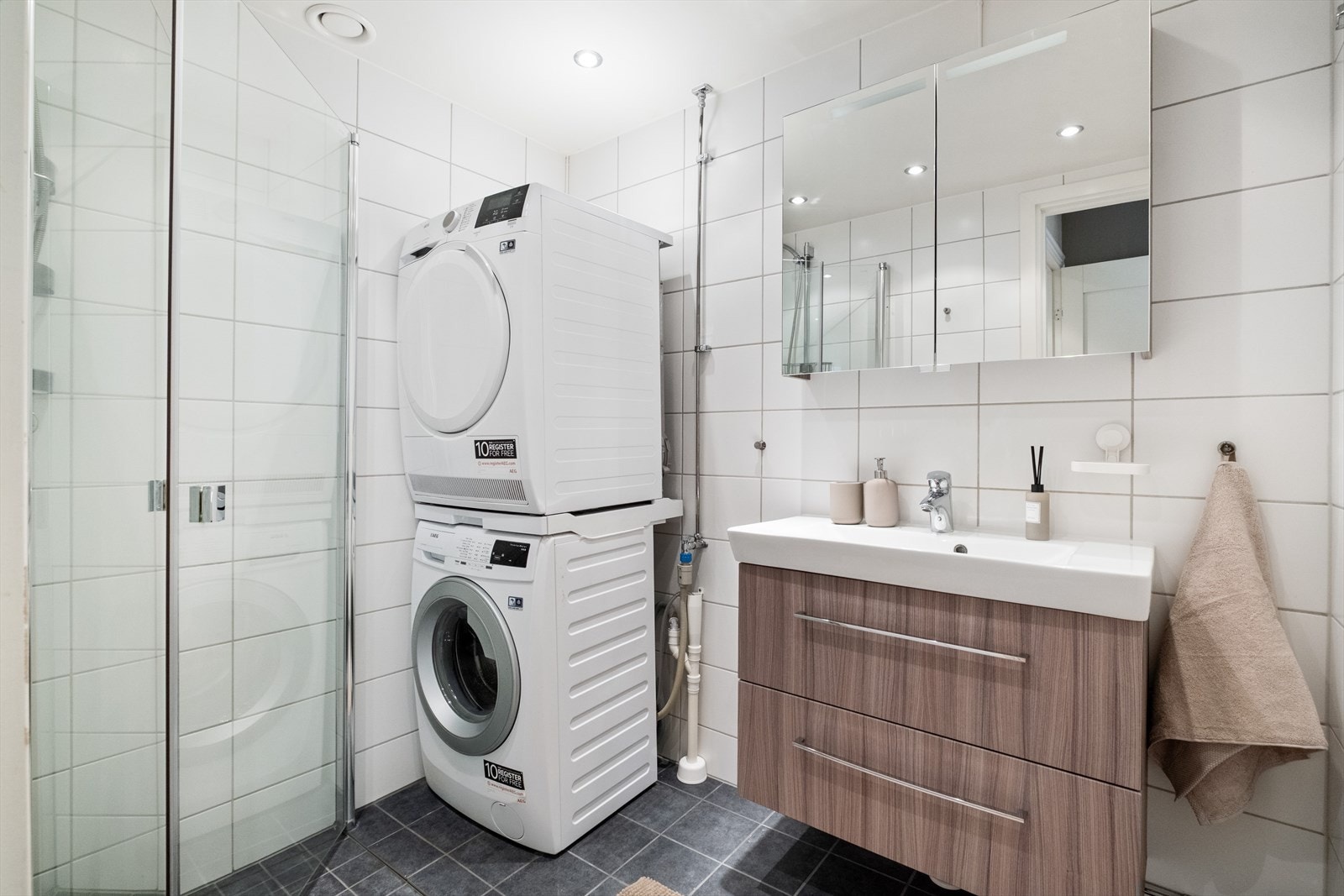 Pent flislagt bad med tidløse, hvite fliser på veggene og mørke fliser på gulvet med varmekabler. Galleribilde