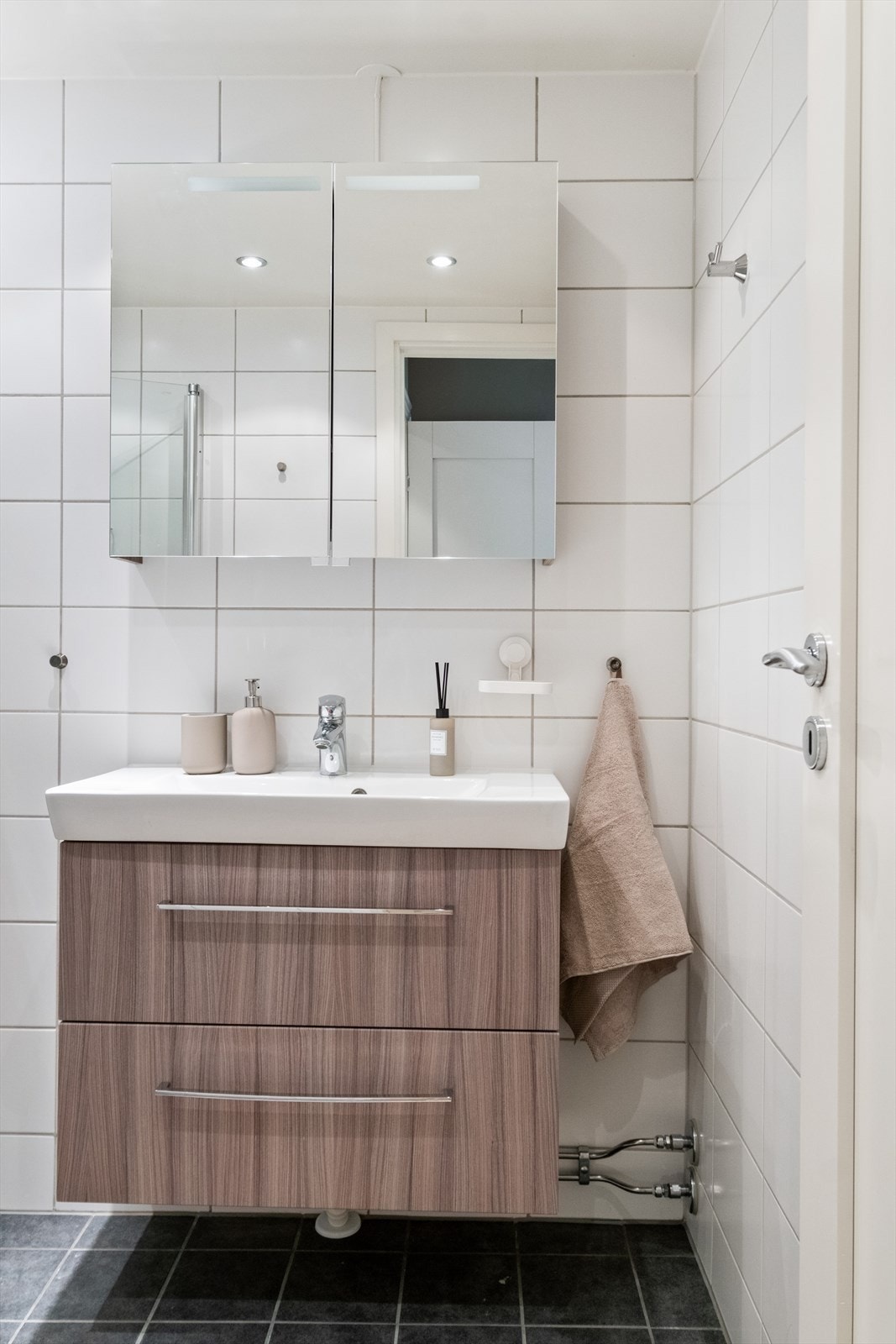 Badet er innredet med nedfelt servant, speil med belysning og dusjhjørne med håndholdt dusjarmatur og dusjvegger. Galleribilde