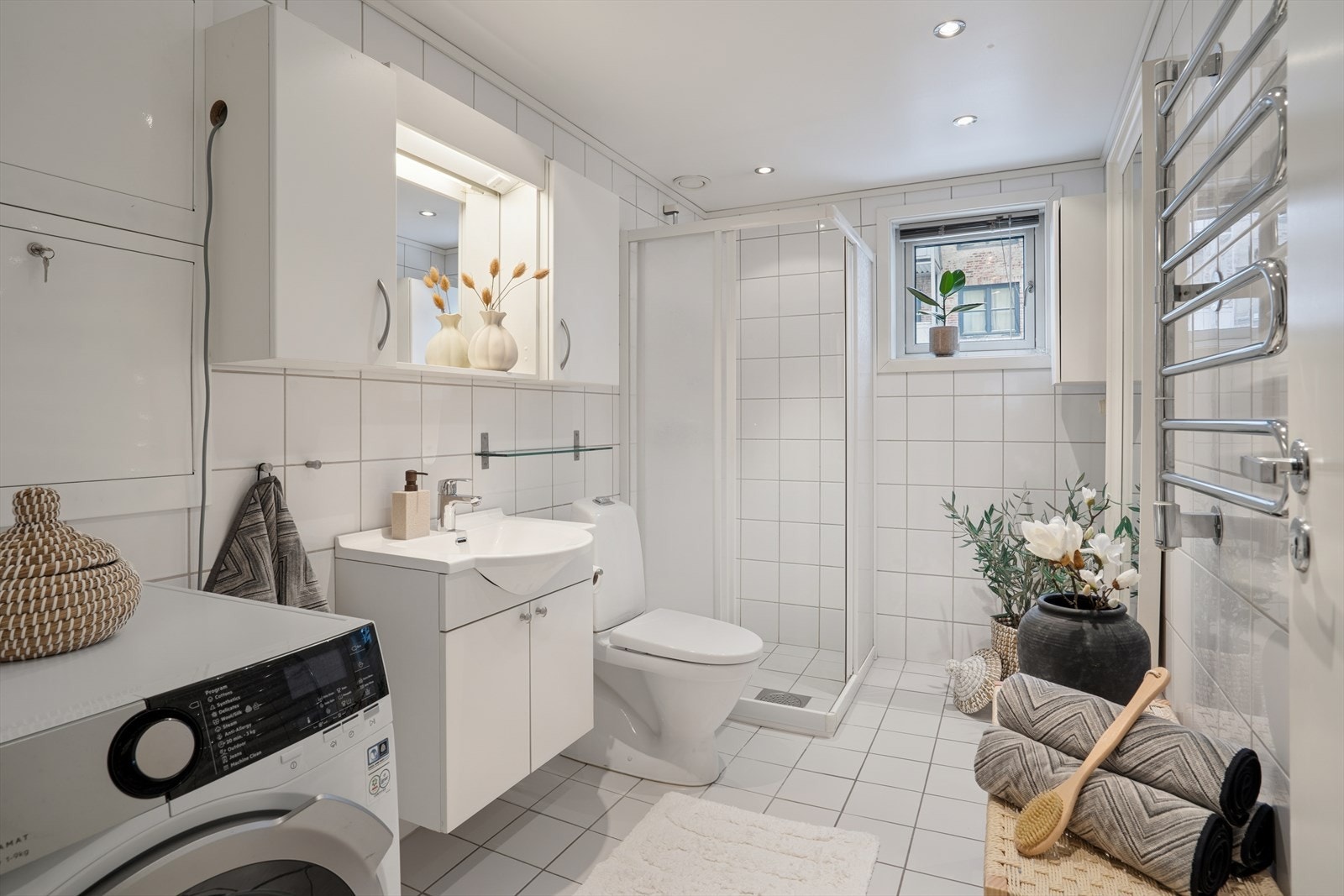 Rommet er innredet med dusjhjørne med glassvegger og dusjgarnityr, et gulvmontert toalett og et praktisk servantskap som gir gode oppbevaringsmuligheter. Opplegg for vaskemaskin gjør i tillegg rommet funksjonelt i hverdagen. Galleribilde