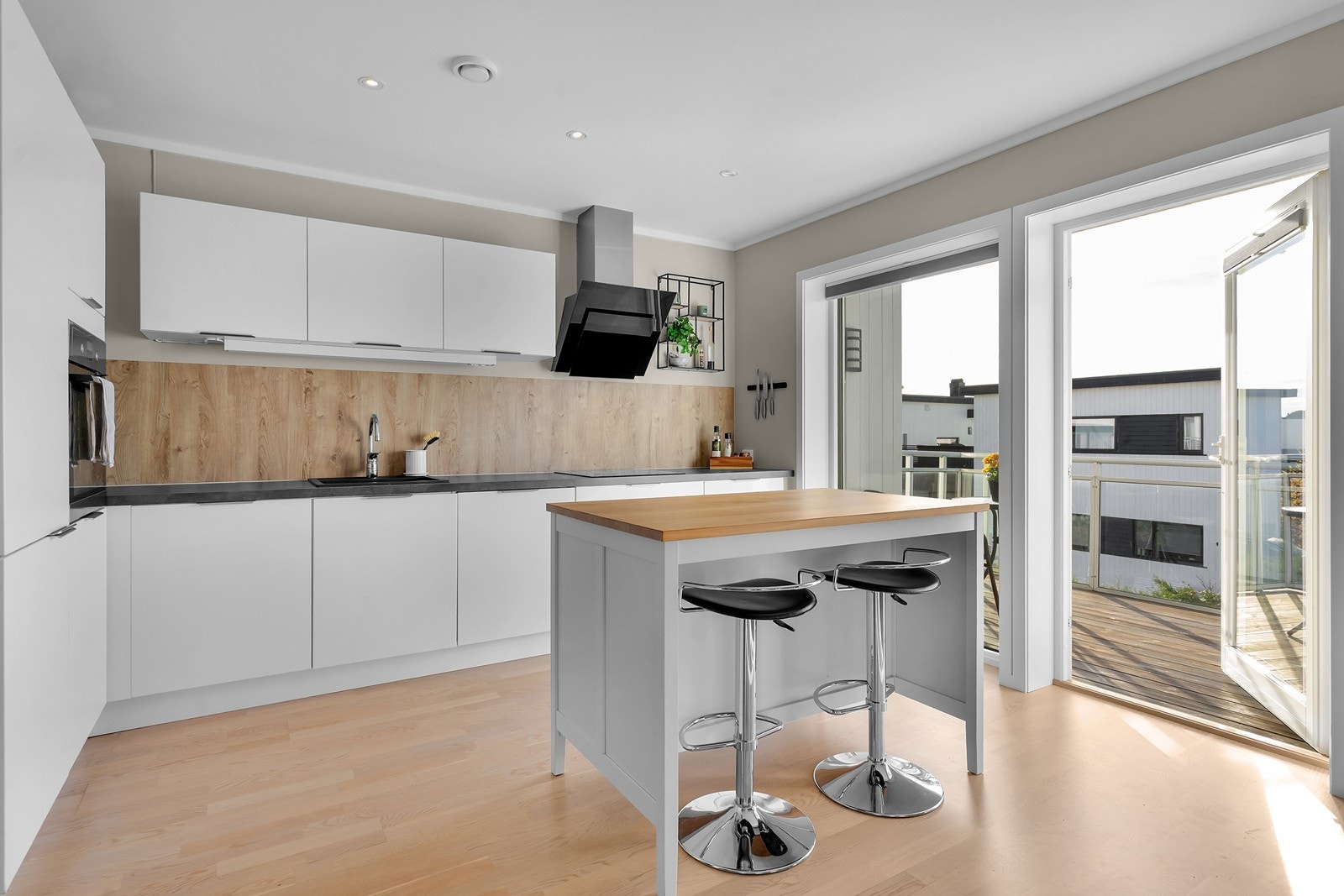 Moderne kjøkken med stilrene fronter, praktisk kjøkkenøy og utgang til solrik veranda. Galleribilde