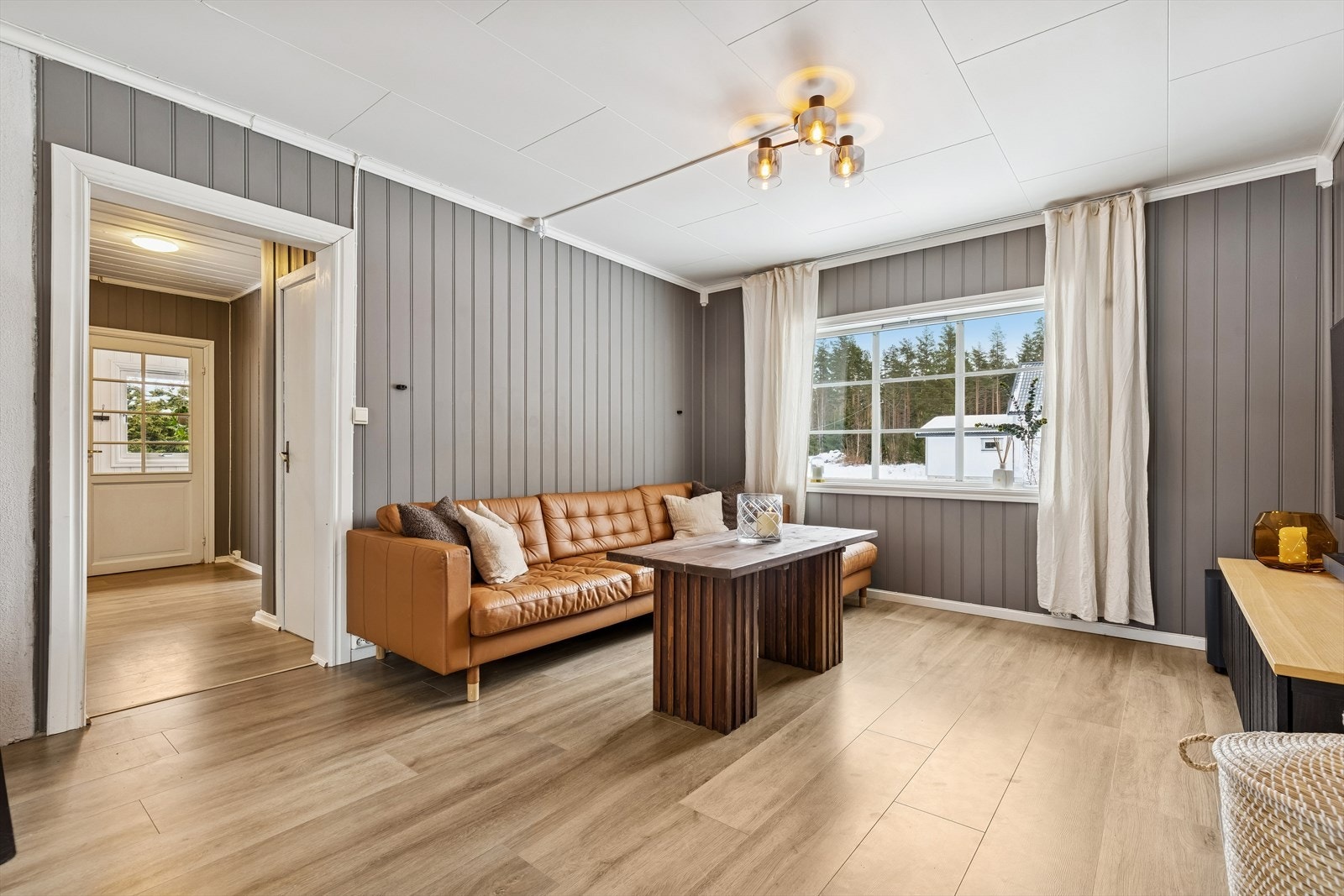 Romslig stue med laminatgulv fra 2021 og vegger kledd med trepanel. Galleribilde