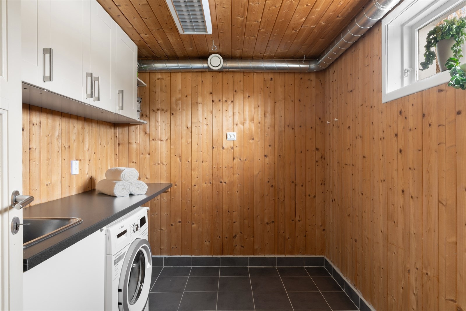 Vaskerom med fliser på gulv og panel på vegg. Rommet er innredet med skaper og en god benkeplate (Ikke byggemeldt til vaskerom). Galleribilde