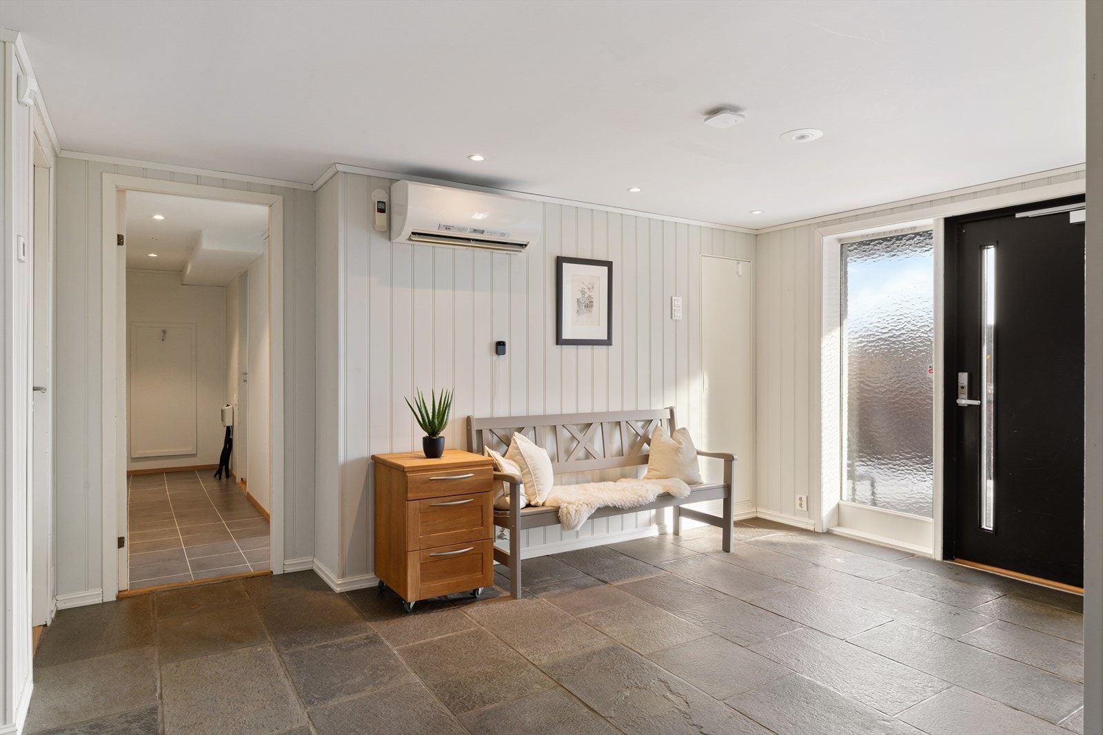 Romslig entre med skifer på gulv. Det er installert varmepumpe sikrer god temperatur året rundt. Det er adkomst til boligens underetasje, med tre soverom og boder på én side, og bad, hobbyrom/bi-inngang og vaskerom på den andre. Galleribilde