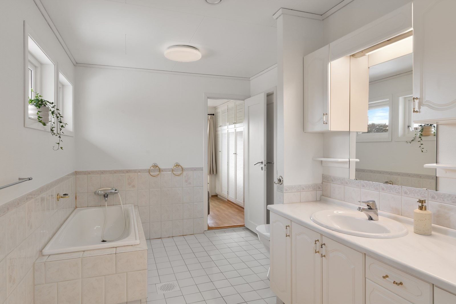 Flislagt bad innredet med badekar, toalett og vask i seksjon. Galleribilde