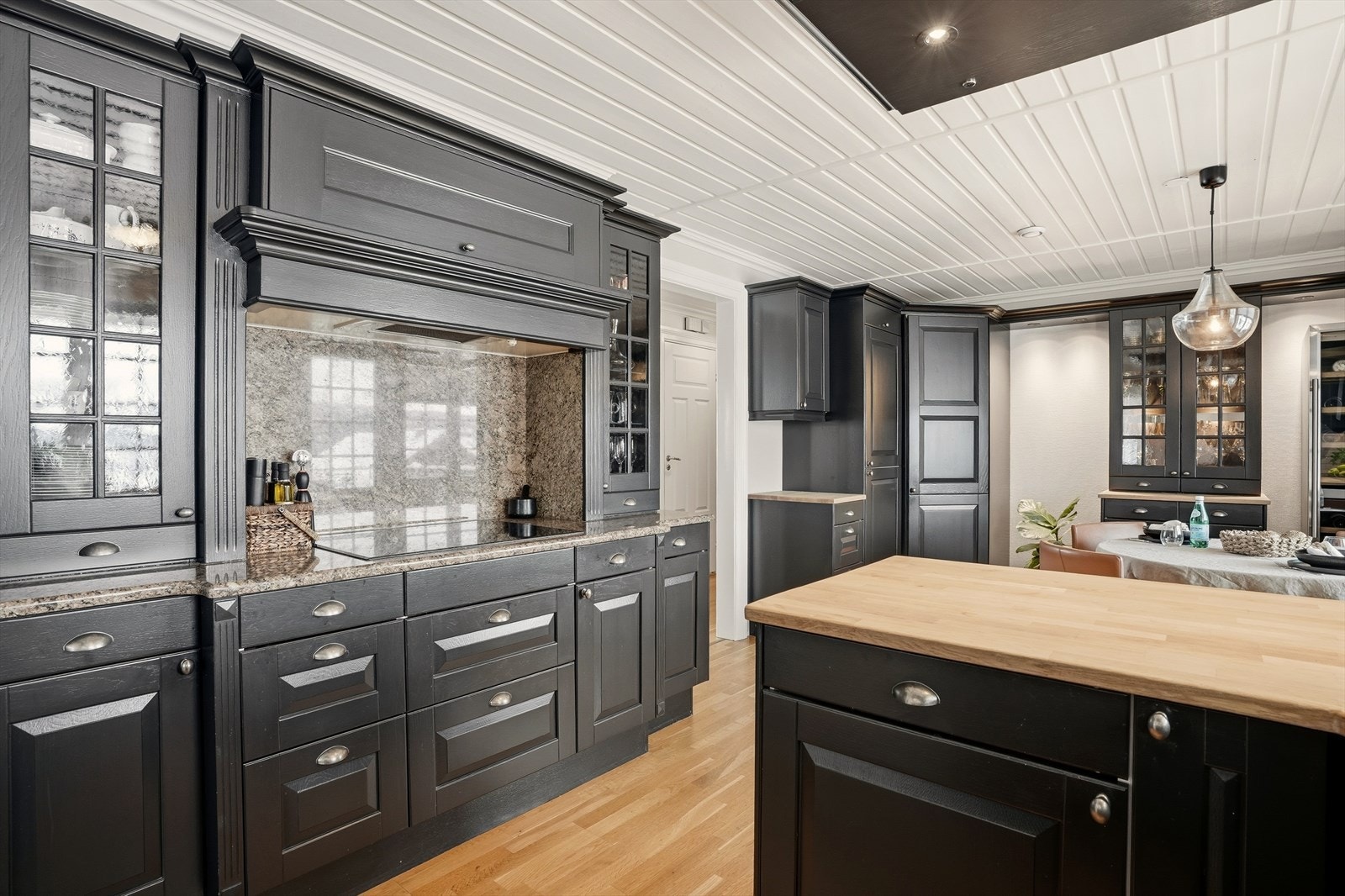 I nisje mot vegg har man en lekker nedfelt induksjonsplatetopp, med ventilator over og med lyssatte vitrineskapsdører på sidene. Overflatene rundt kokesonen er steinsatt, hvilket gir et slitesterkt og robust kjøkken over tid. Galleribilde