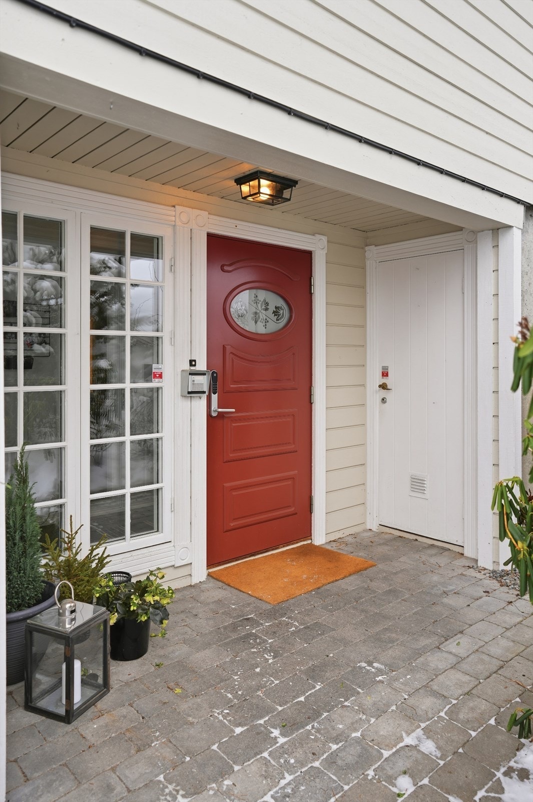 Boligen har et hyggelig takoverbygd inngangsparti. Her er steinlagt gangsti opp fra garasjen, og til høyre for inngangsdøra har man et egen sportsbod. Galleribilde