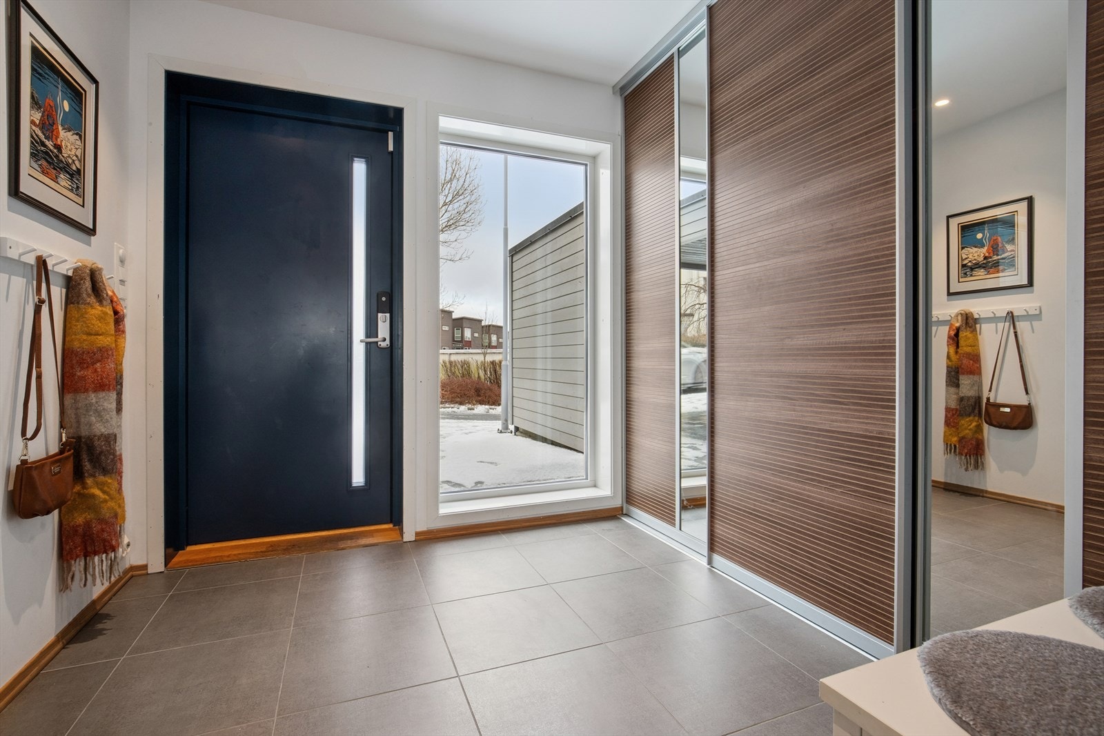 Flislagt entré med plass til stor skyvedørsgarderobe og annet møblement. Galleribilde
