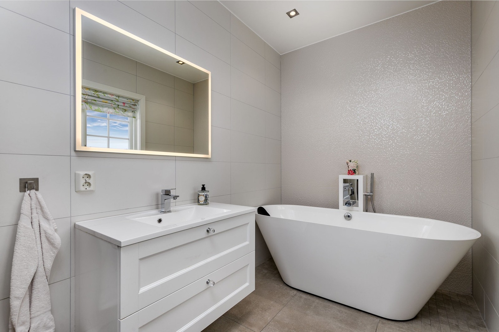 Badet i boligens første etasje er pent flislagt med gulvvarme og ble pusset opp av fagfolk i 2016. Innredningen består av profilert servantinnredning, speil, vegghengt toalett, samt frittstående ovalt badekar med dusjløsning. Galleribilde