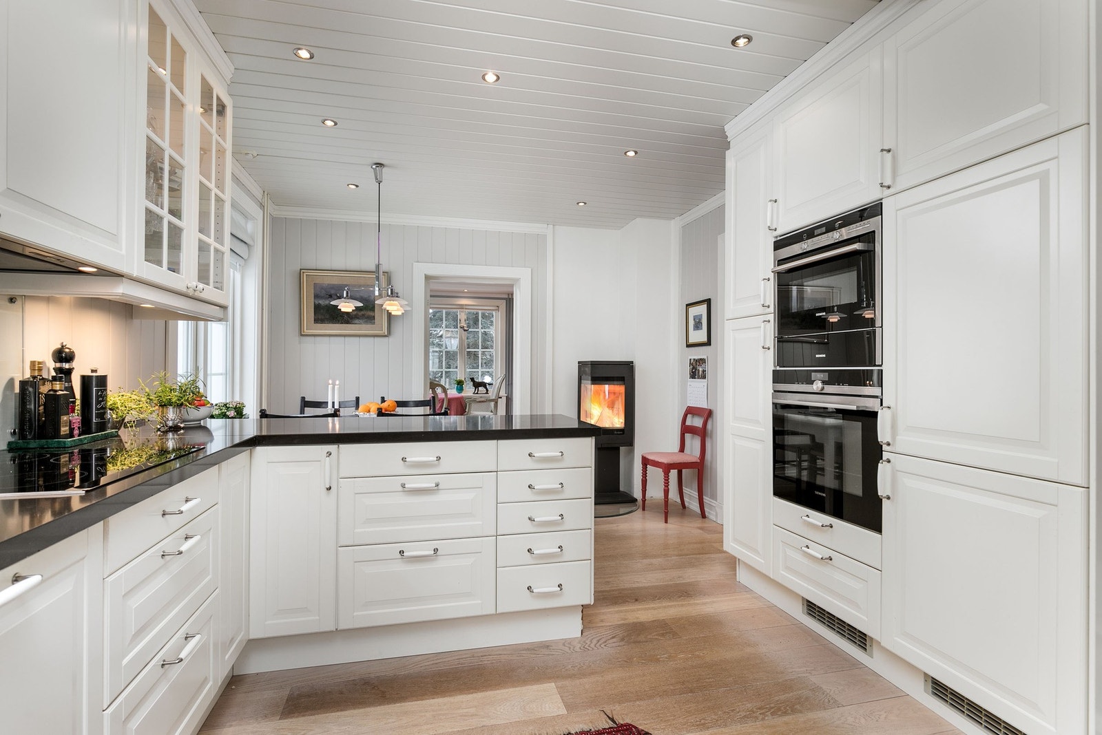 Innredningen består av profilerte kremhvite fronter i kombinasjon med opplyste vitrineskap og benkeplate i eksklusiv steinkompositt med nedfelt vaskekum. Galleribilde