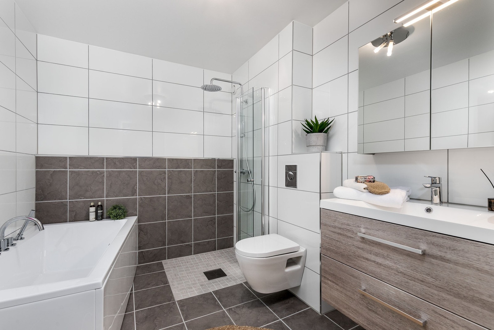 Videre har badet et dusjhjørne med innfellbare glassdører og regnfallsdusj, samt et frittstående badekar. Galleribilde