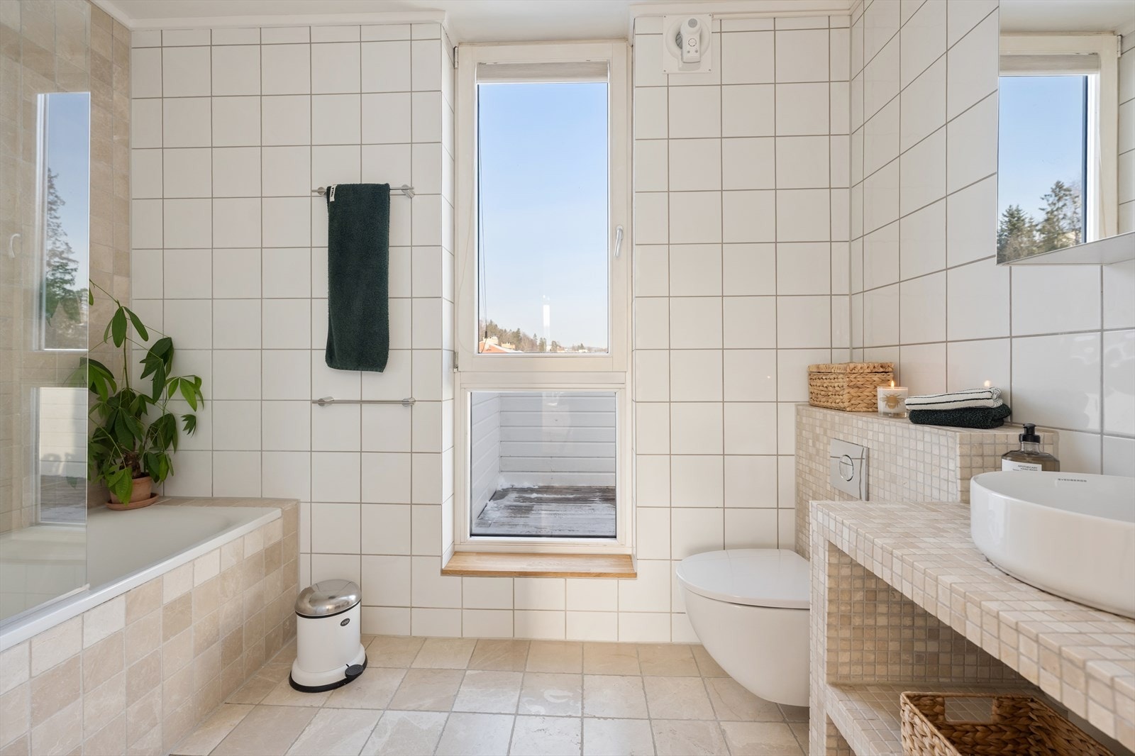 Badet er innredet med servant på innredning med hyller under. Speilskap over servant. Vegghengt toalett. Badekar med dusjløsning og glassvegg Galleribilde