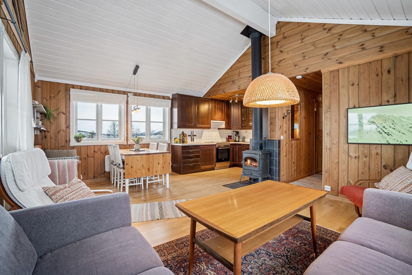 Lun og trivelig stue med store vinduer, vedovn og åpen løsning mot kjøkkenet. Galleribilde