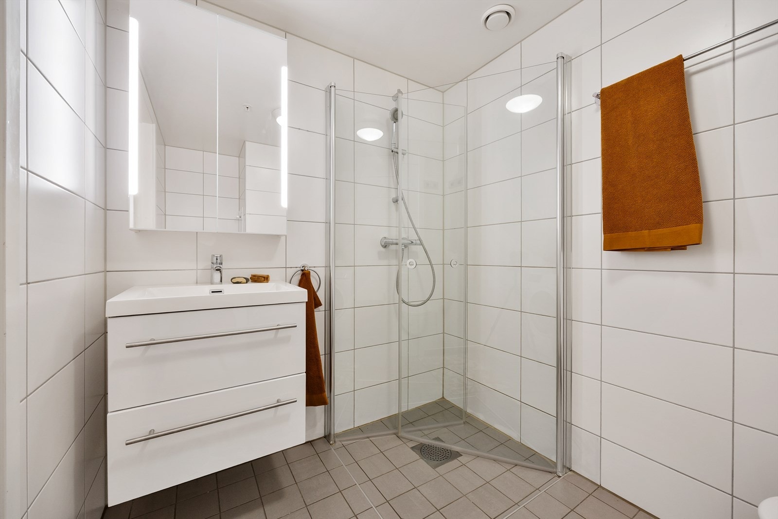 Badet er innredet med servant, speilskap og dusjhjørne med dører i herdet glass. Galleribilde