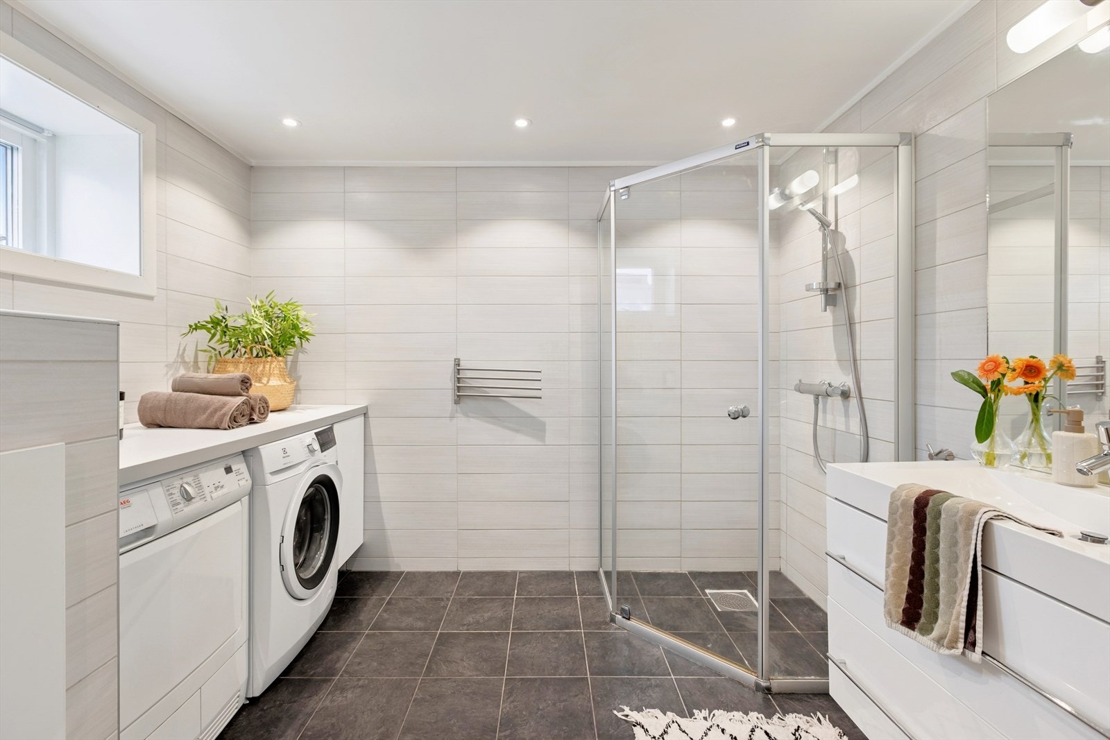 Badet er romslig og utstyrt med dusj og lys innredning med god skuffeplass. Det er opplegg for vask/tørk med benkeplate som en praktisk løsning, samt spotter i taket. Galleribilde