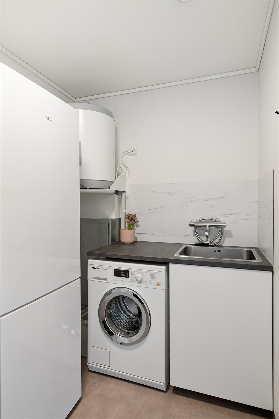 Vaskerom/teknisk rom med plass til ekstra fryseskap. Utslagsvask og benkeplate med skap under vask. Belegg på gulv. Rør klargjort til wc og vask, dersom en ønsker toalett i 1.etg. Galleribilde