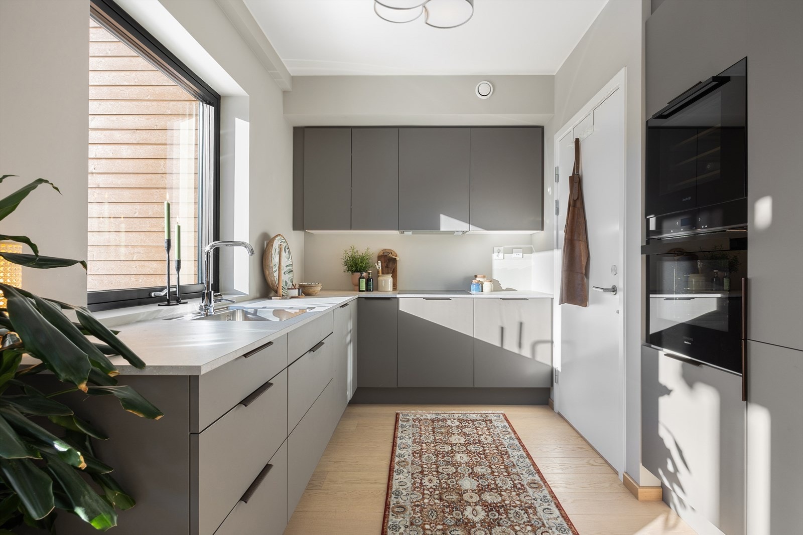 Benkeplate med planlimt kum i kompositt kompletterer kjøkkenets stilrene estetikk. Induksjonstopp, stekeovn, oppvaskmaskin, vinskap og kjøl/frys er integrert i innredningen. Galleribilde