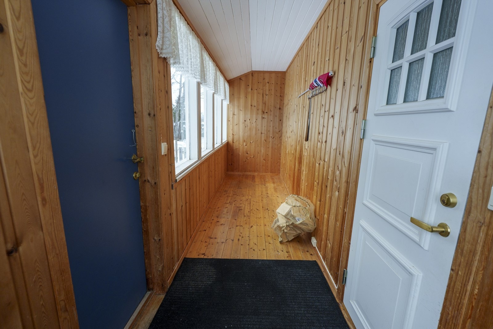 Innglasset inngangsparti med lakkerte heltre gulv, trepanel på veggene og flere vinduer som slipper inn flott lys. Galleribilde