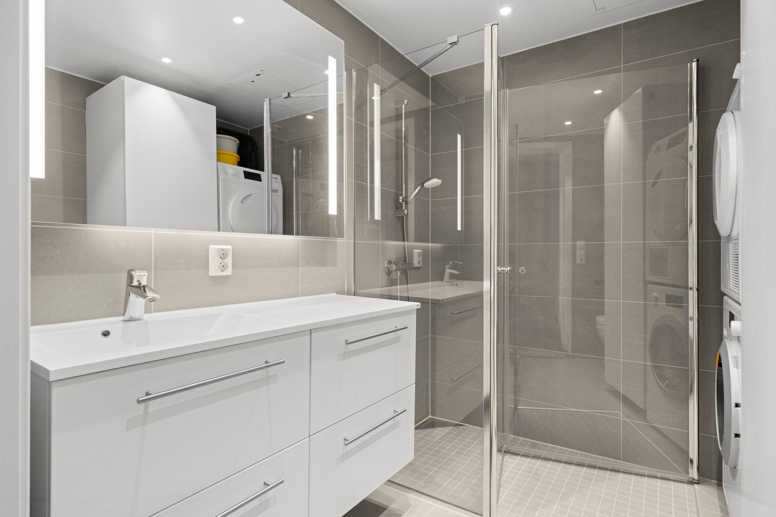 Baderommet har innredning med nedfelt servant, veggmontert toalett, dusjvegger/hjørne og opplegg for vaskemaskin. Galleribilde