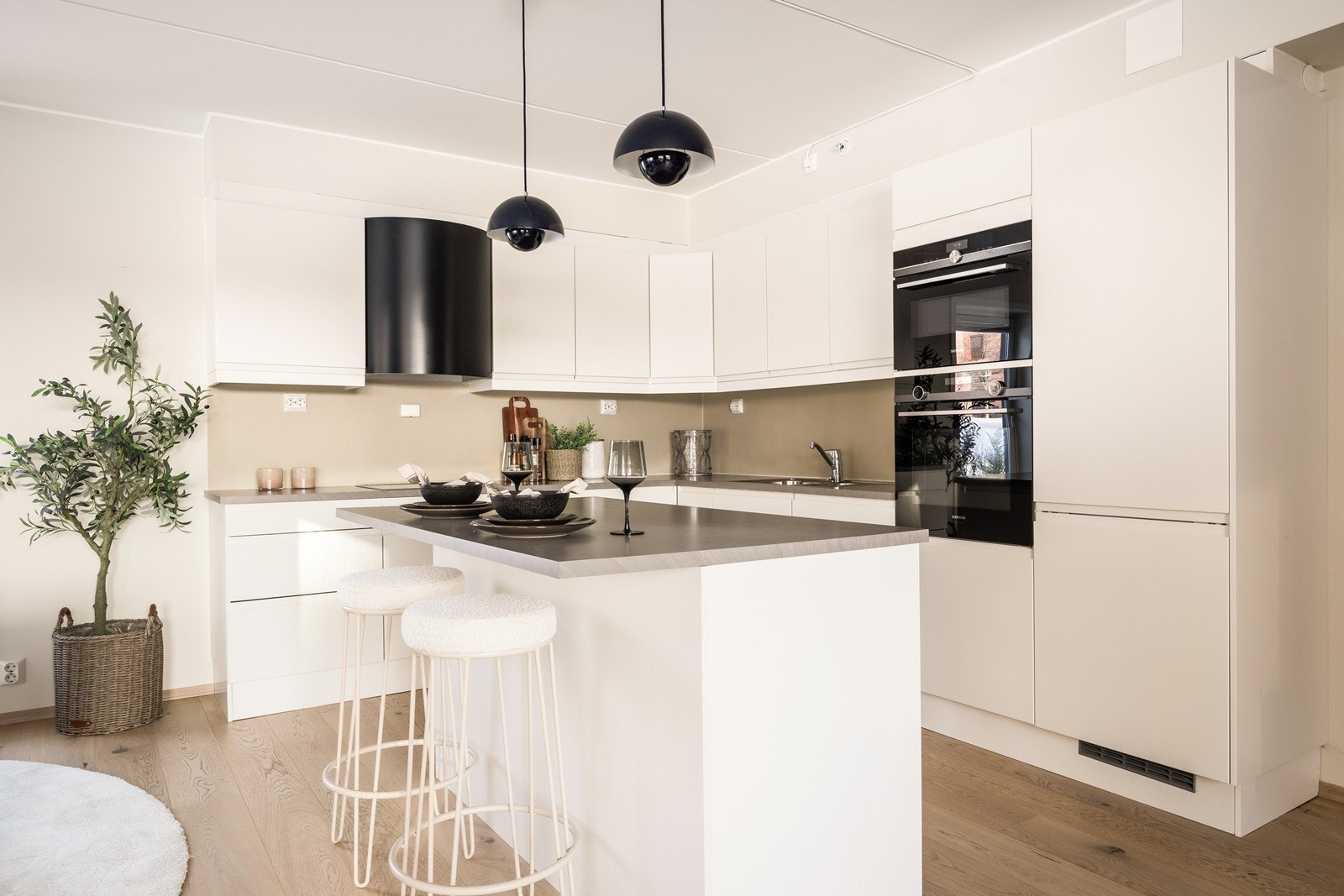 Hjørnekjøkken med praktisk øy i midten. Hvite glatte fronter, rikelig med benkeplass, samt integrerte hvitevarer. Galleribilde