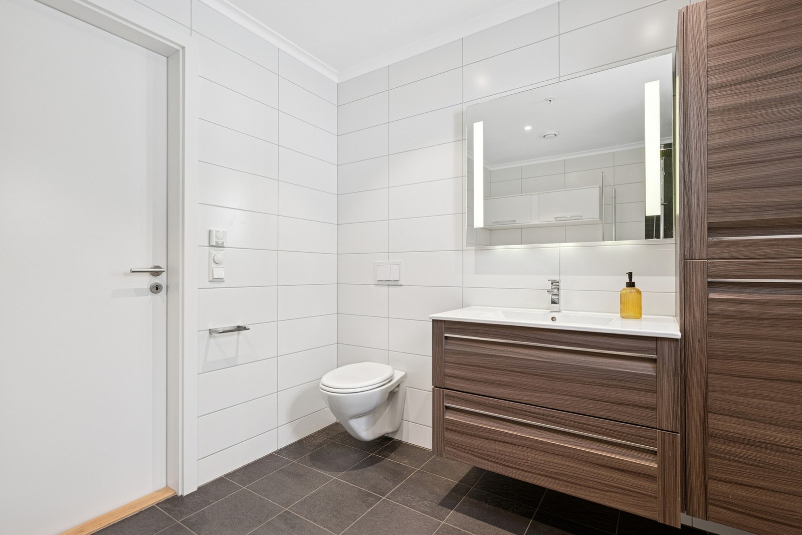 Badet er innredet med vegghengt servant og tilhørende høyskap, samt vegghengt toalett med innebygget sisterne. Galleribilde