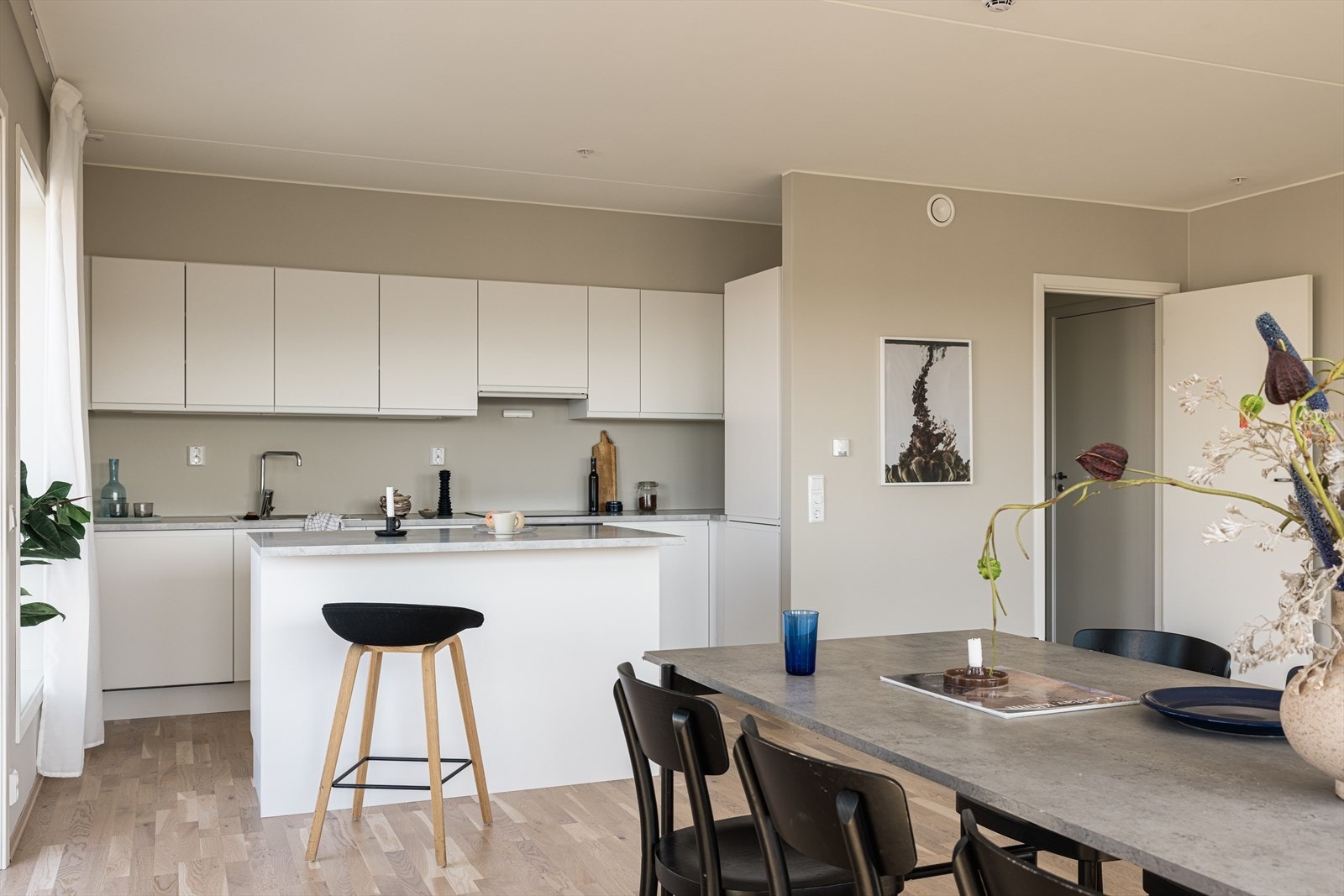 Kjøkkenet ligger diskret plassert, men med naturlig forbindelse til spisestuen. Innredningen er minimalistisk med glatte, hvite fronter og en lys grå benkeplate, og byr på god oppbevaringsplass i både over- og underskap. Galleribilde